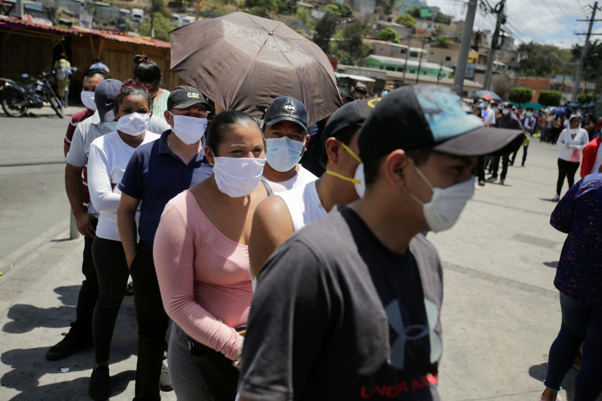 Ciudadanos de Honduras hacen cola en la puerta de un supermercado de Tegucigalpa protegidos con mascarillas ante la extensión del coronavirus.
