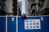 Un hombre con mascarilla se asoma por una barricada en Wuhan.