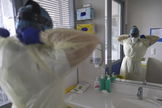 Una enfermera de una UCI belga se pone su EPI ante el espejo.