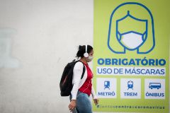 Una joven camina frente a un letrero que recomienda el uso de mascarillas en Sao Paulo.