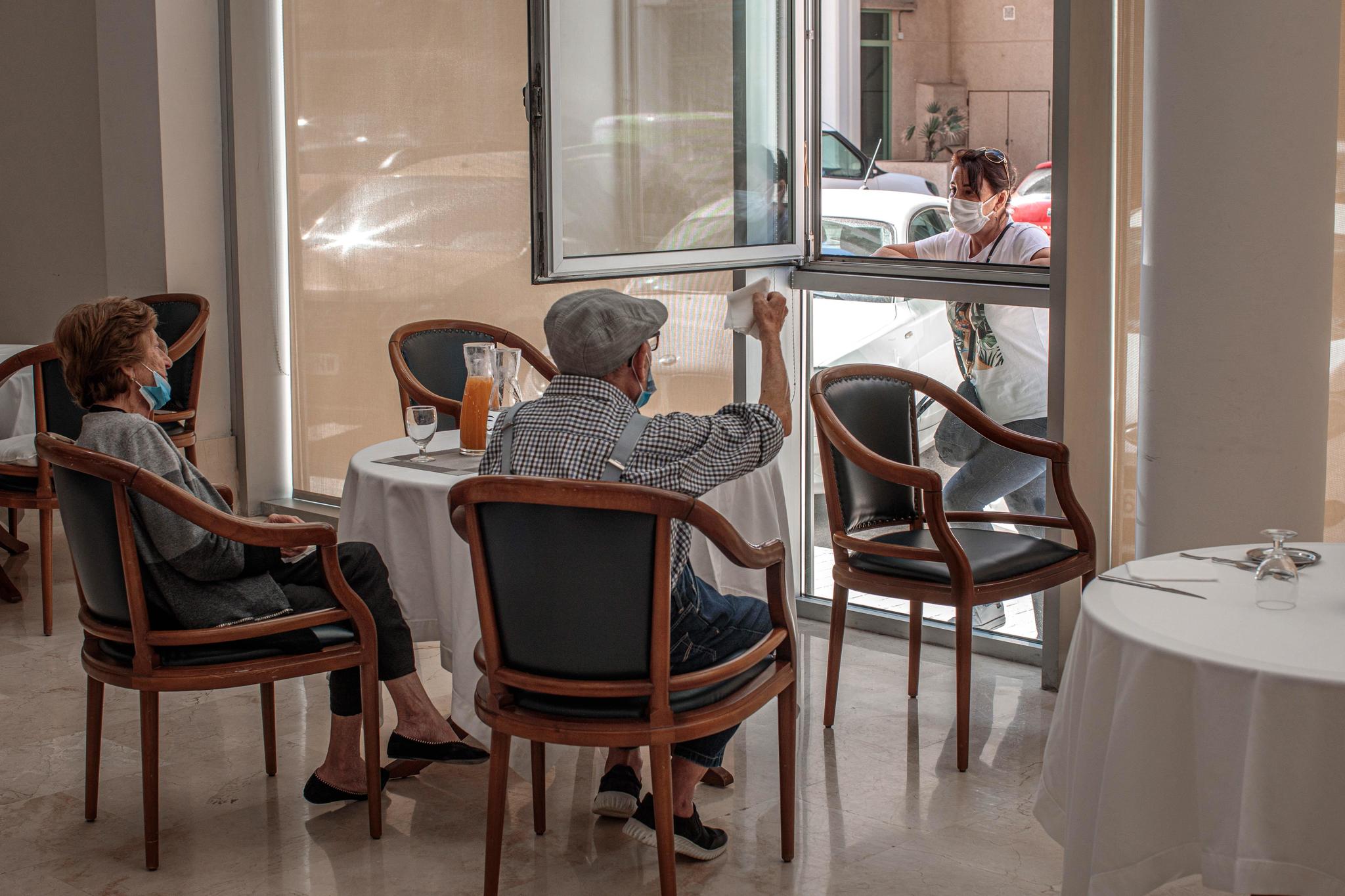 Dos residentes charlan con un familiar por la ventana del centro de mayores.