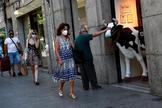 Un hombre acaricia la figura de una vaca con mascarilla en el centro de Madrid