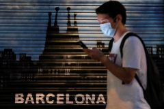 Un hombre con mascarilla pasa frente a un cartel en Barcelona | REUTERS