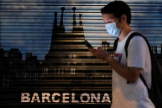Un hombre con mascarilla pasa frente a un cartel en Barcelona | REUTERS