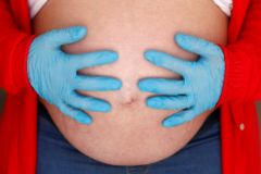Una embarazada de nueves meses se palpa la tripa con guantes.
