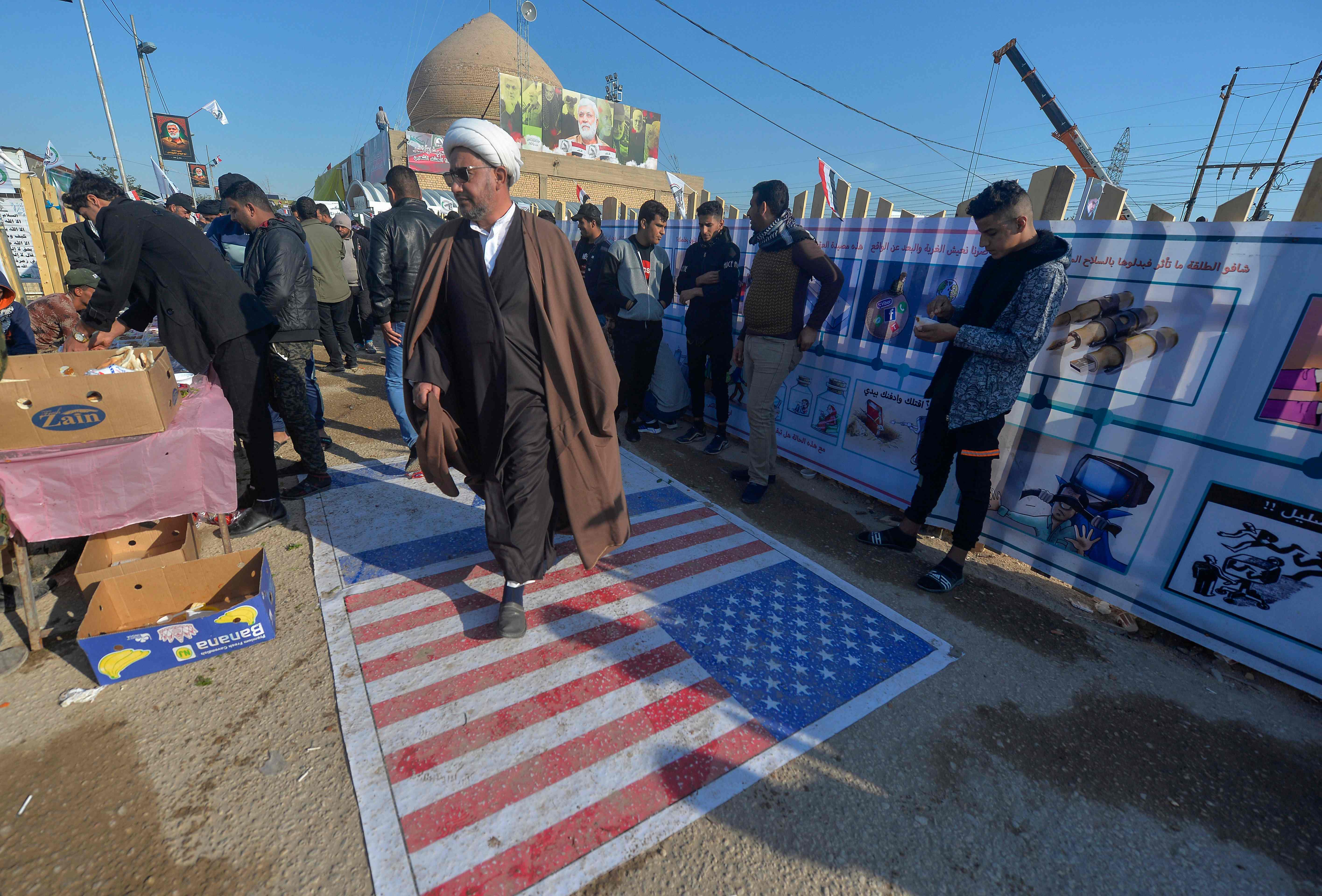 Un clrigo iraqu camina sobre una bandera estadounidense durante un homenaje a un comandante asesinado junto a Qasem Soleimani.