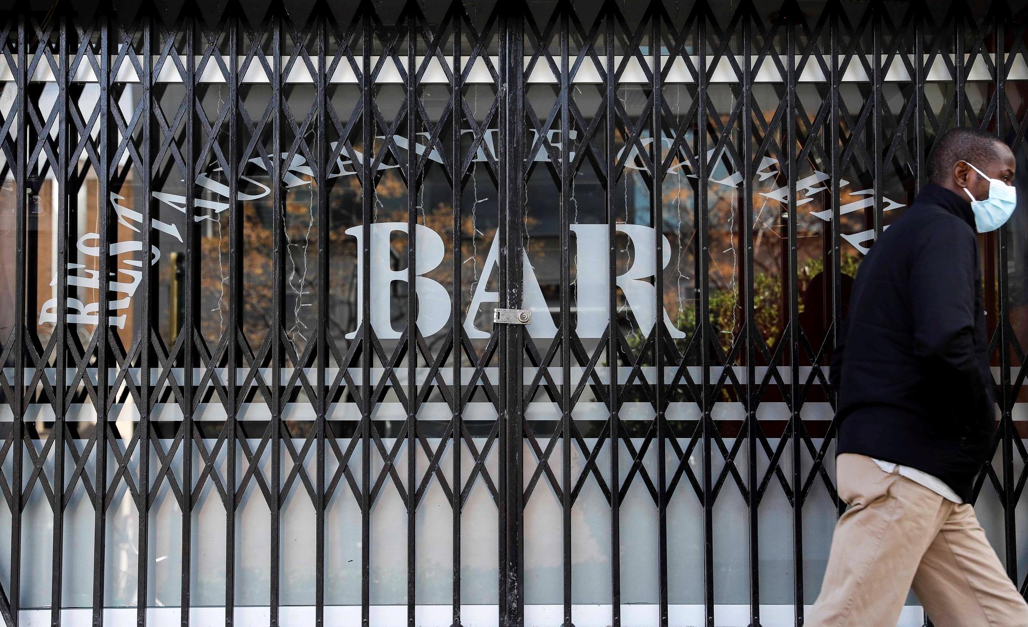 Una persona pasa por delante de un bar que permanece cerrado en Valencia la pandemia de coronavirus.