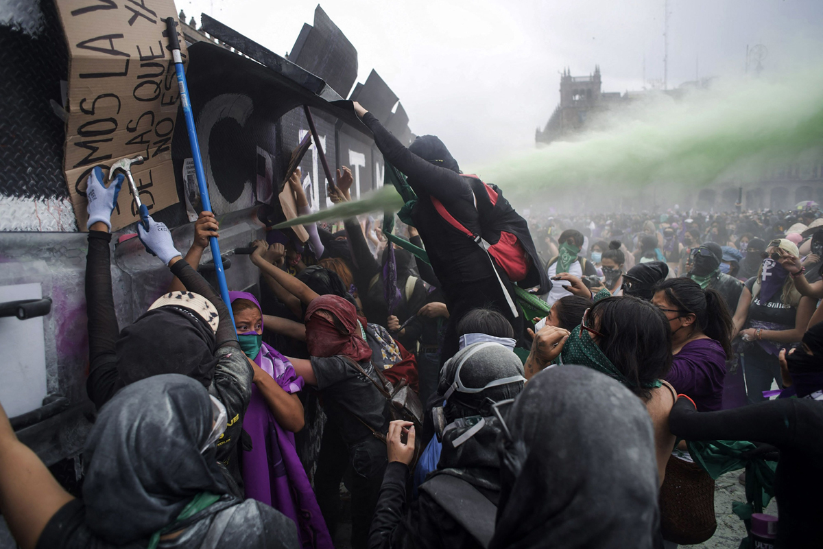 Mujeres intentan derribar la barrera de seguridad del Palacio Nacional en las protestas del 8-M.