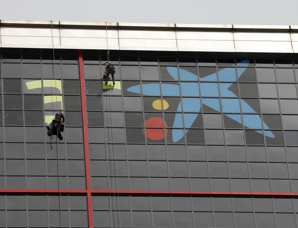 Varios operarios instalan el logo de CaixaBank en las madrileas Torres Kio.