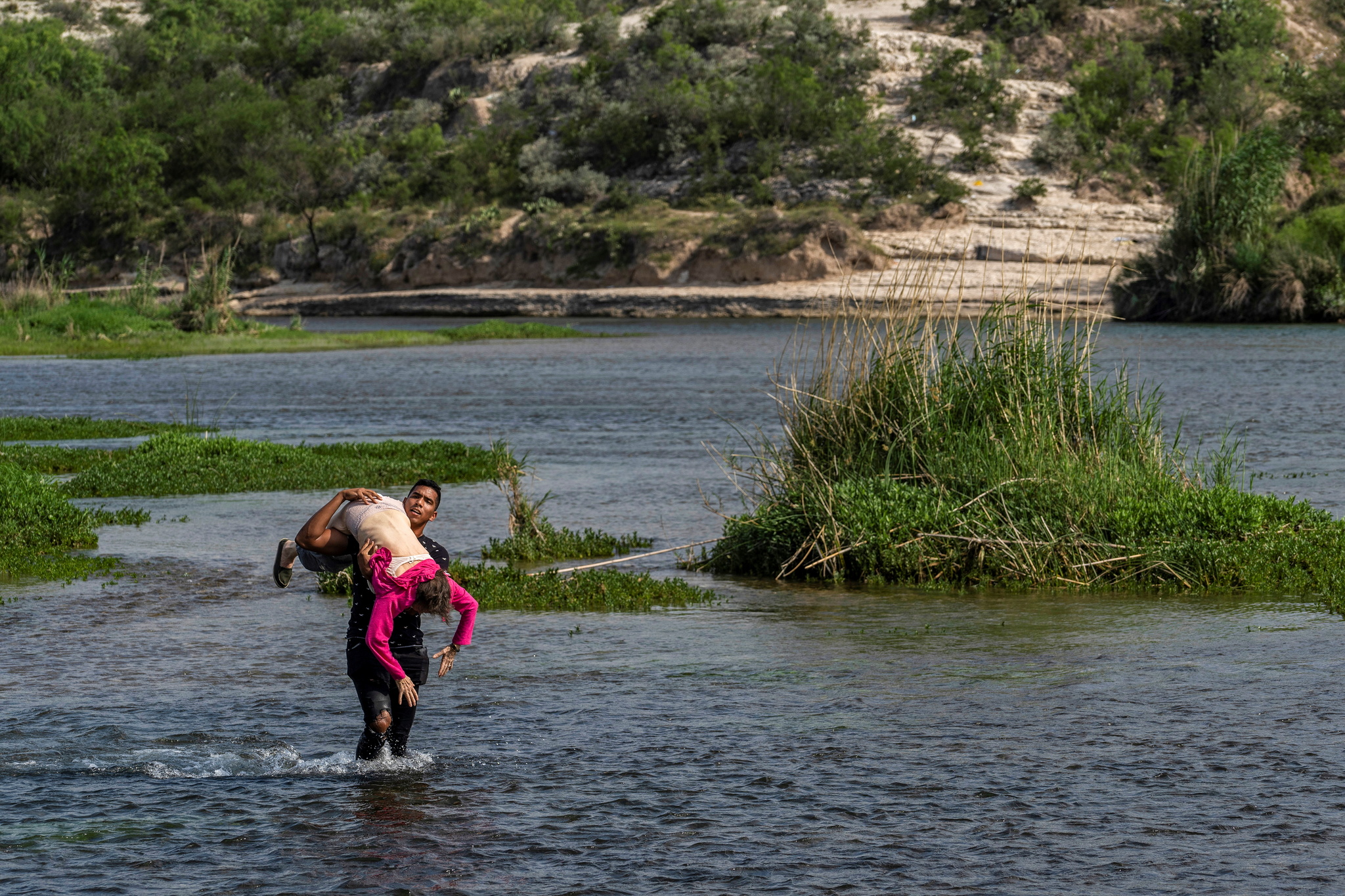 Un migrante cruza la frontera entre EEUU y Mxico con una anciana en brazos.