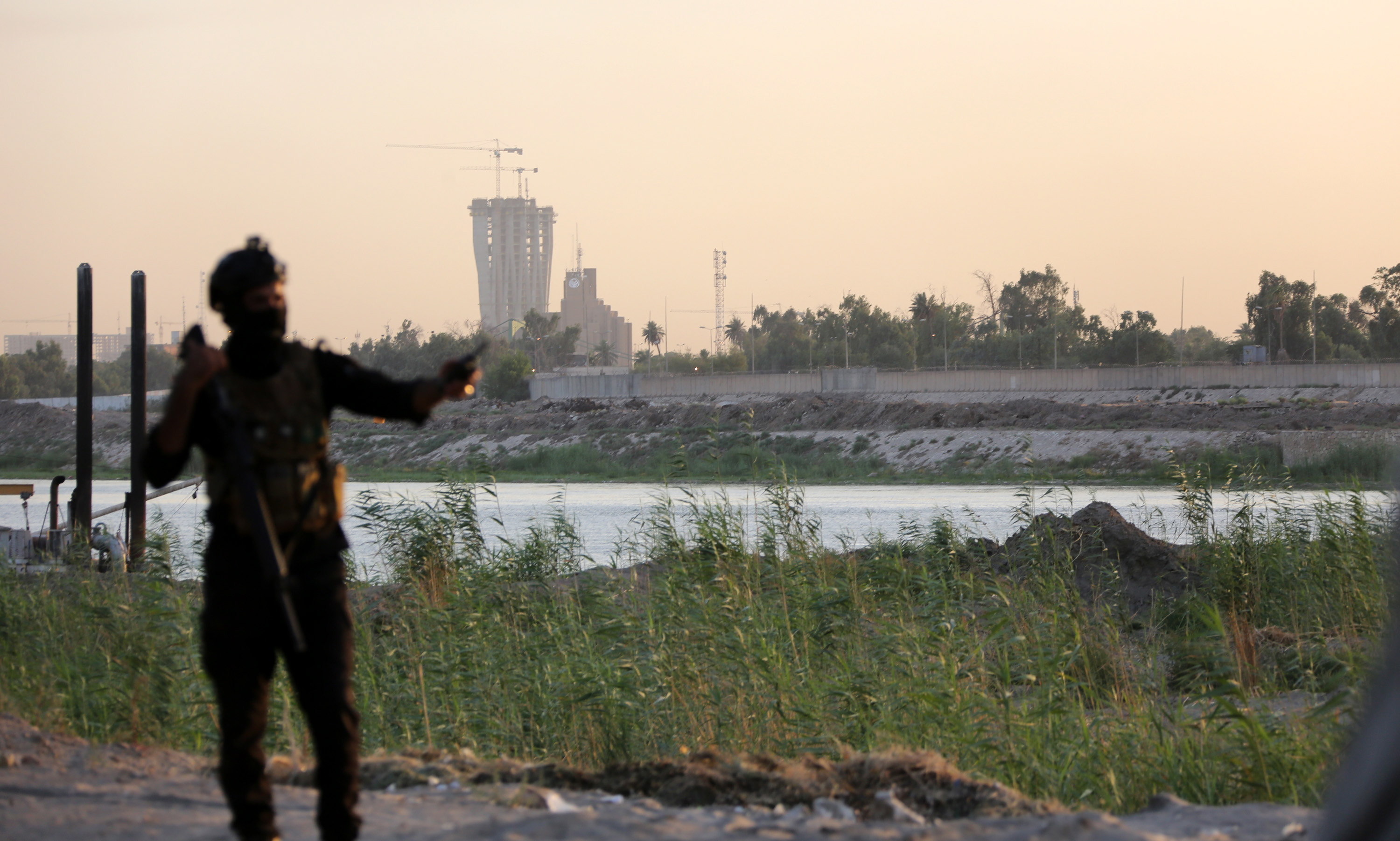 Un miembro de las fuerzas especiales iraquíes monta guardia con la fuertemente fortificada Zona Verde, que alberga las oficinas del gobierno iraquí y la embajada de Estados Unidos y otras misiones diplomáticas internacionales, al fondo, en el centro de Bagdad.