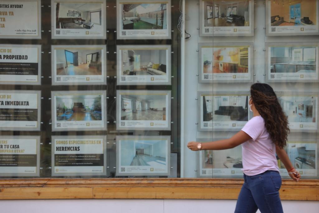 Una mujer camina ante un escaparate lleno de anuncios de viviendas en venta y alquiler.