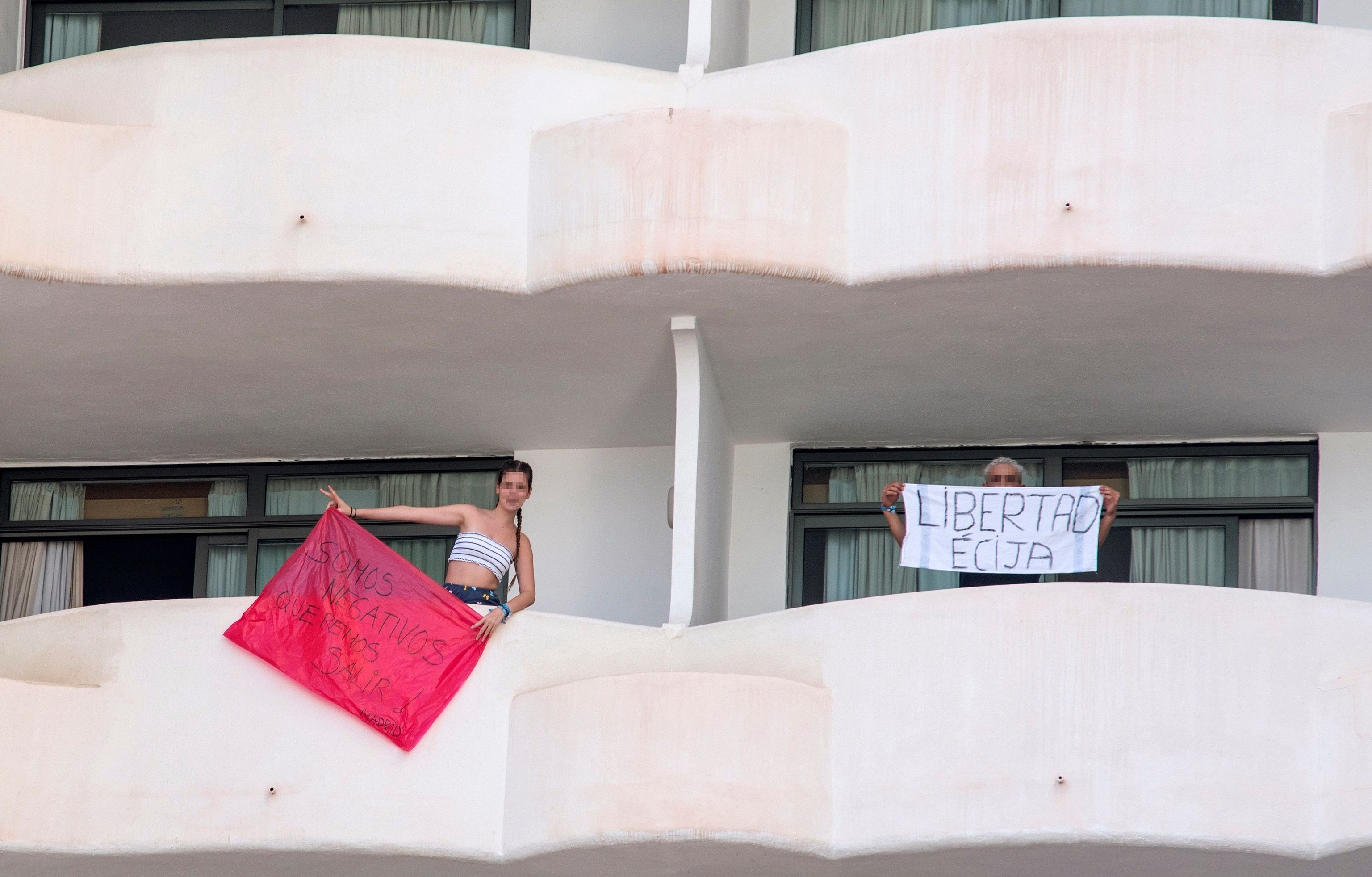 Dos jóvenes que permanecen en aislamiento en el hotel Palma Bellver de Palma portan dos pancartas pidiendo salir del hotel. EFE/ Atienza