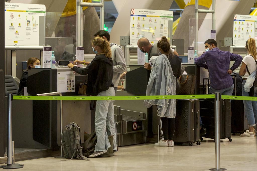 Varios pasajeros entregan sus documentos para viajar desde el aeropuerto de Barajas.