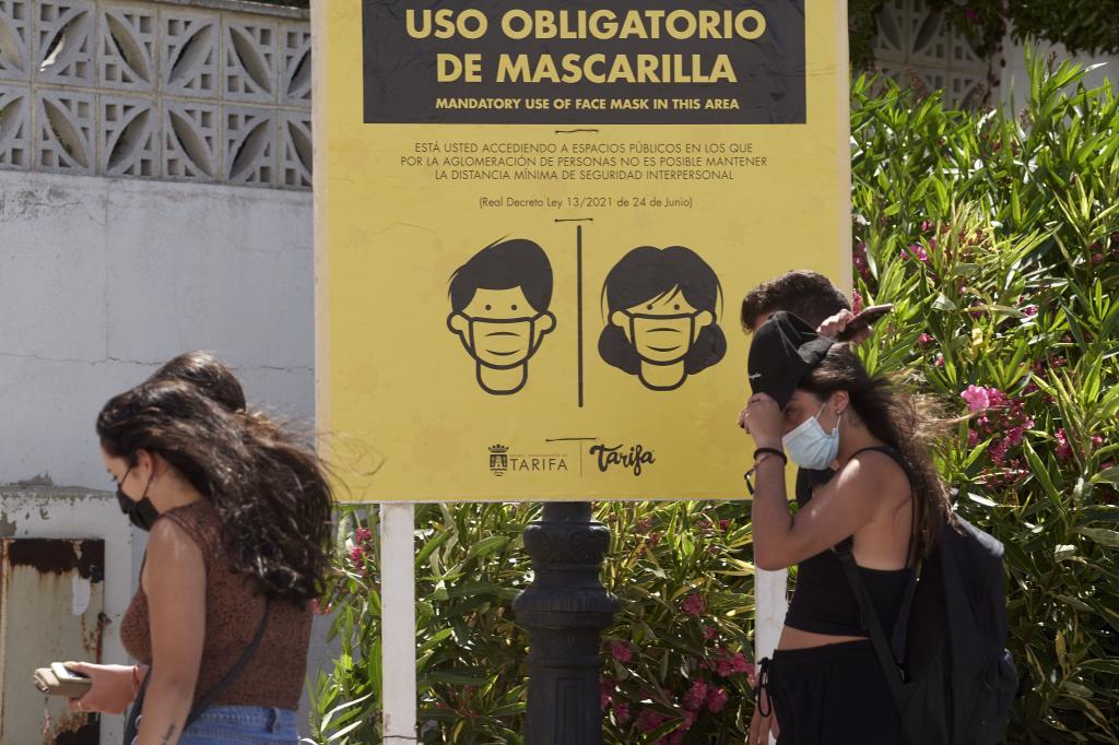 Un grupo de jvenes turistas pasa en Tarifa junto a un cartel que insta al uso de la mascarilla ante la alta incidencia del virus.