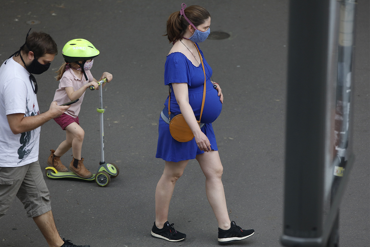 Mujer embarazada caminando con mascarilla.