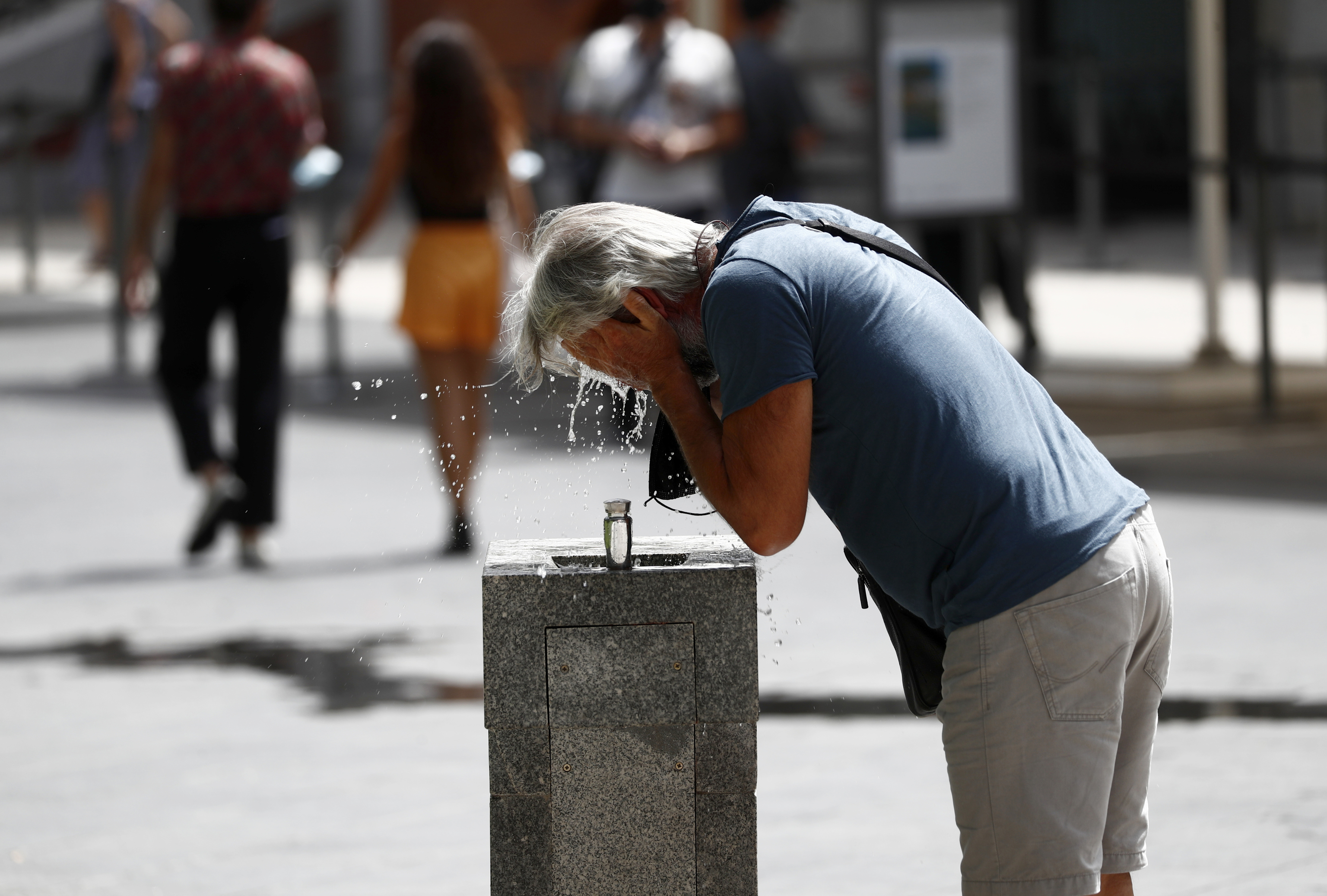 Un hombre, junto al museo del Prado, se refresca en una fuente.