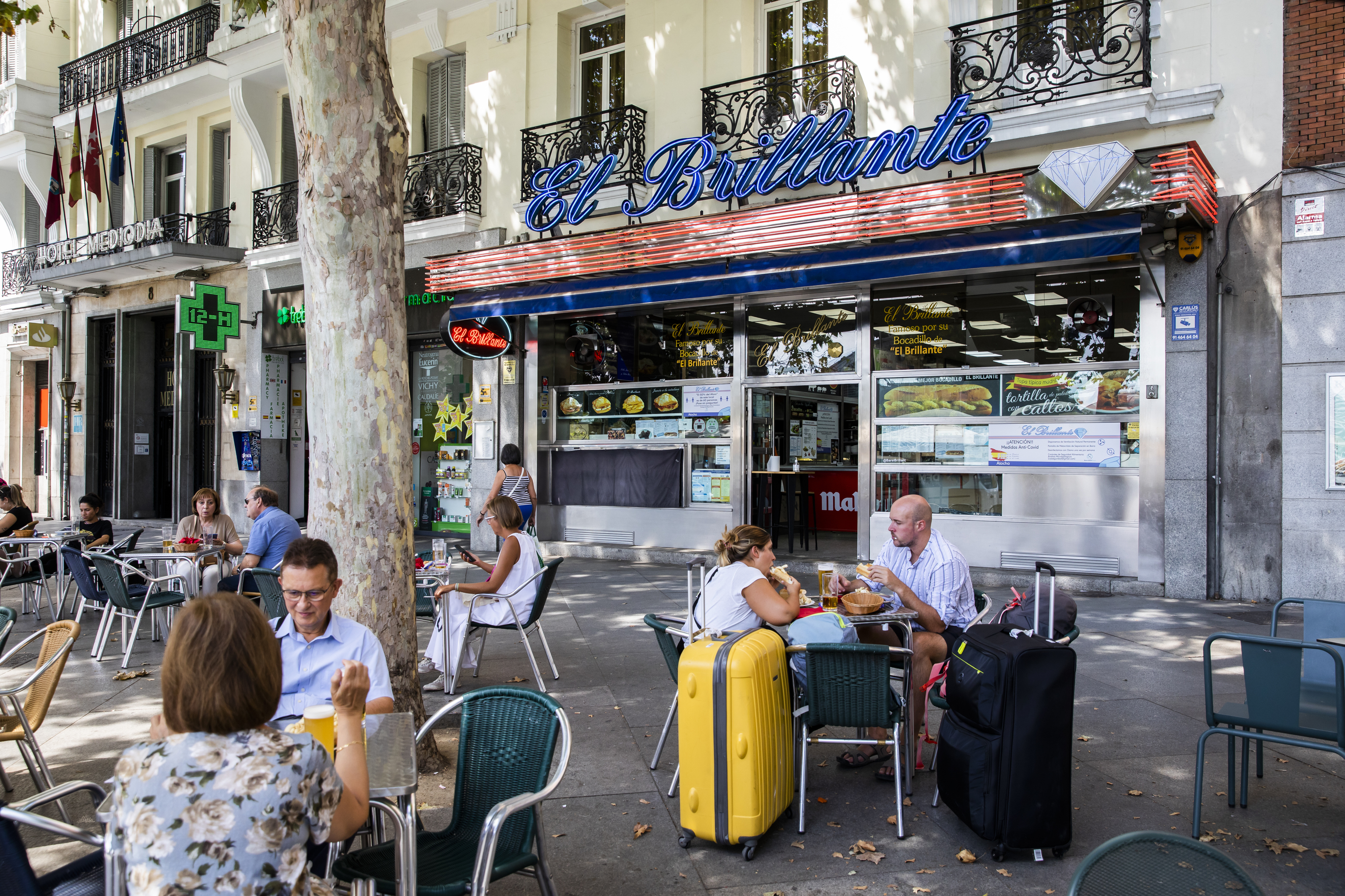 Ciudadanos, algunos con maletas, disfrutan de la terraza de un bar de la plaza del Emperador Carlos V, en Madrid.