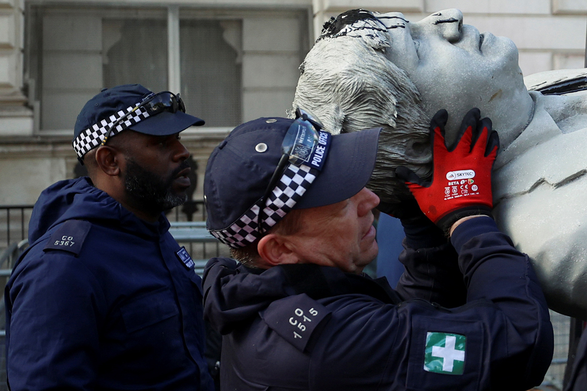Dos policías trasladan una estatua vandalizada de Boris Johnson.