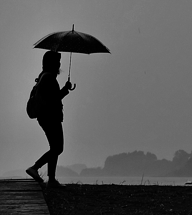 Una mujer pasea mientras sostiene un paraguas, en la playa de A Madalena, en el concello corus de Cabanas.