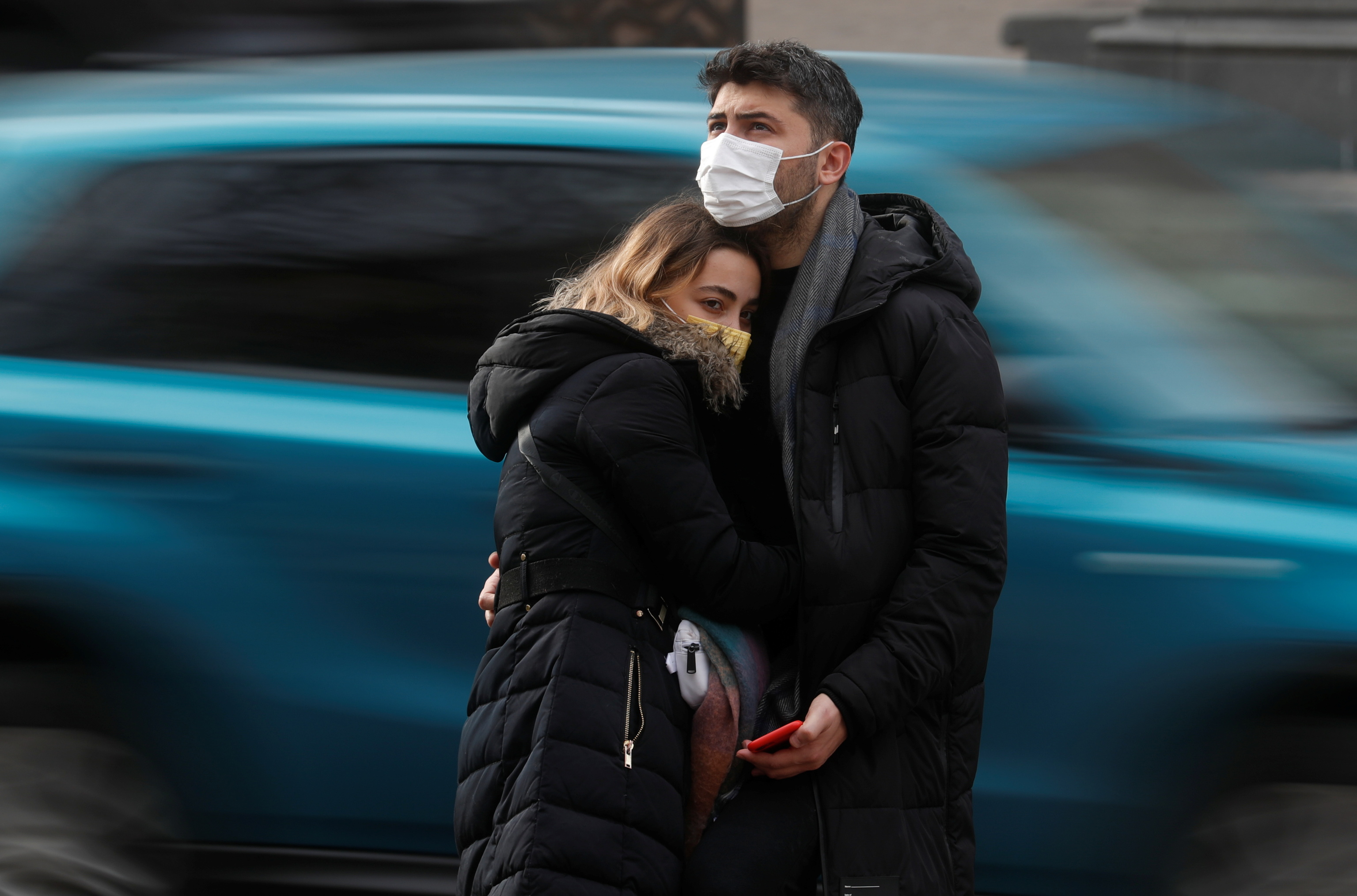 Una pareja lleva mascarillas mientras se abraza en la calle.