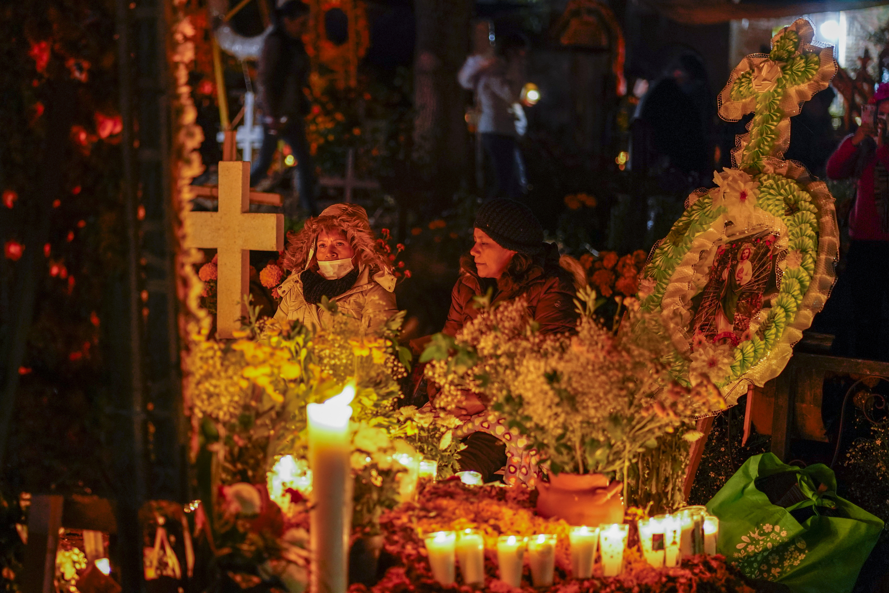 Familiares velan junto a las tumbas durante las festividades del Día de los Muertos en el cementerio de Tzintzuntzan en Michocan, México, el domingo 31 de octubre de 2021. En una tradición que coincide con el Día de Todos los Santos y el Día de los Fieles Difuntos, los días 1 y 2 de noviembre, las familias decoran las tumbas de sus familiares fallecidos con caléndulas y velas, y pasan la noche en el cementerio, comiendo y bebiendo mientras acompañan a sus seres queridos fallecidos.