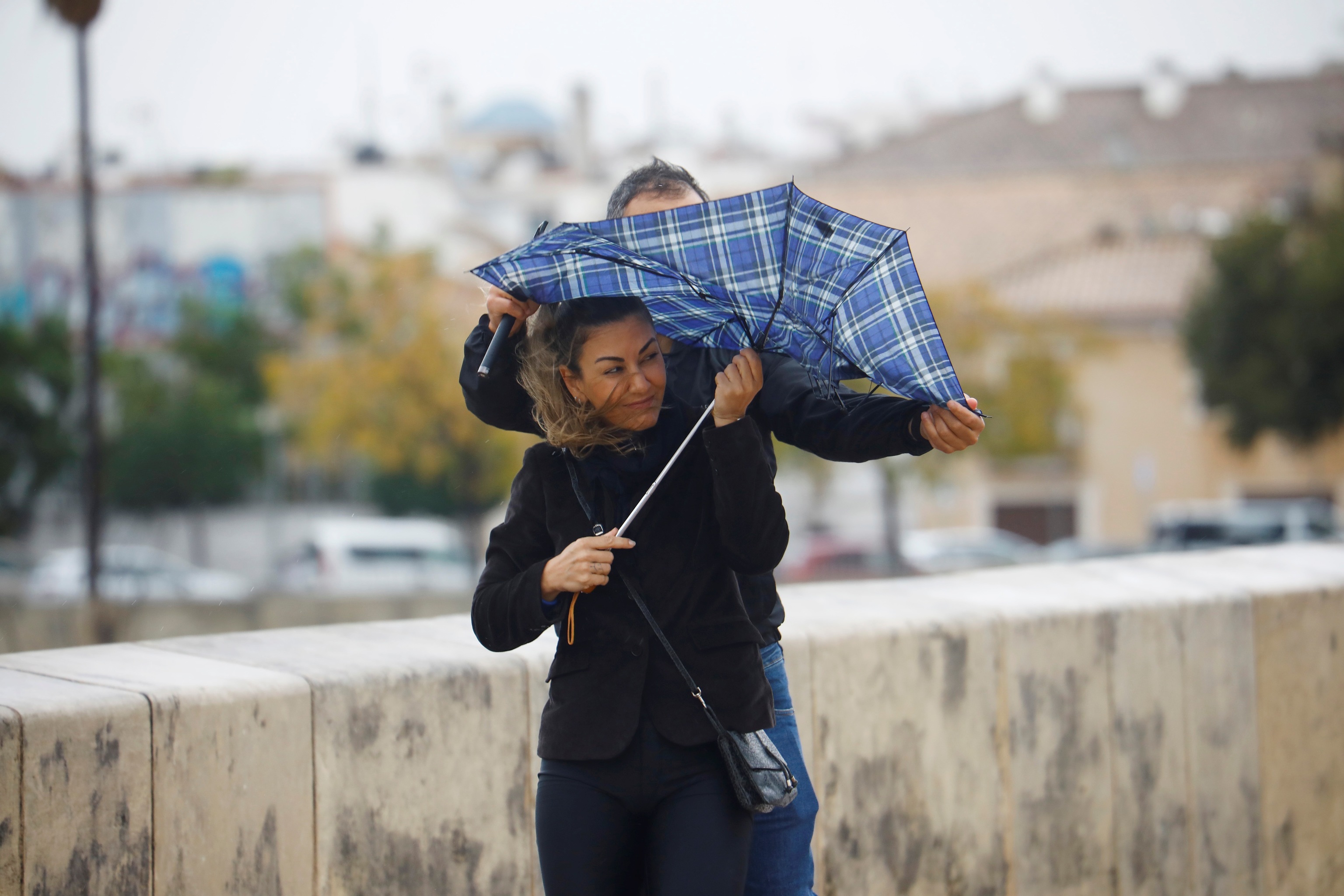Unos turistas intentan protegerse del viento y de la lluvia con un paraguas mientra caminan por el puente romano de Crdoba.