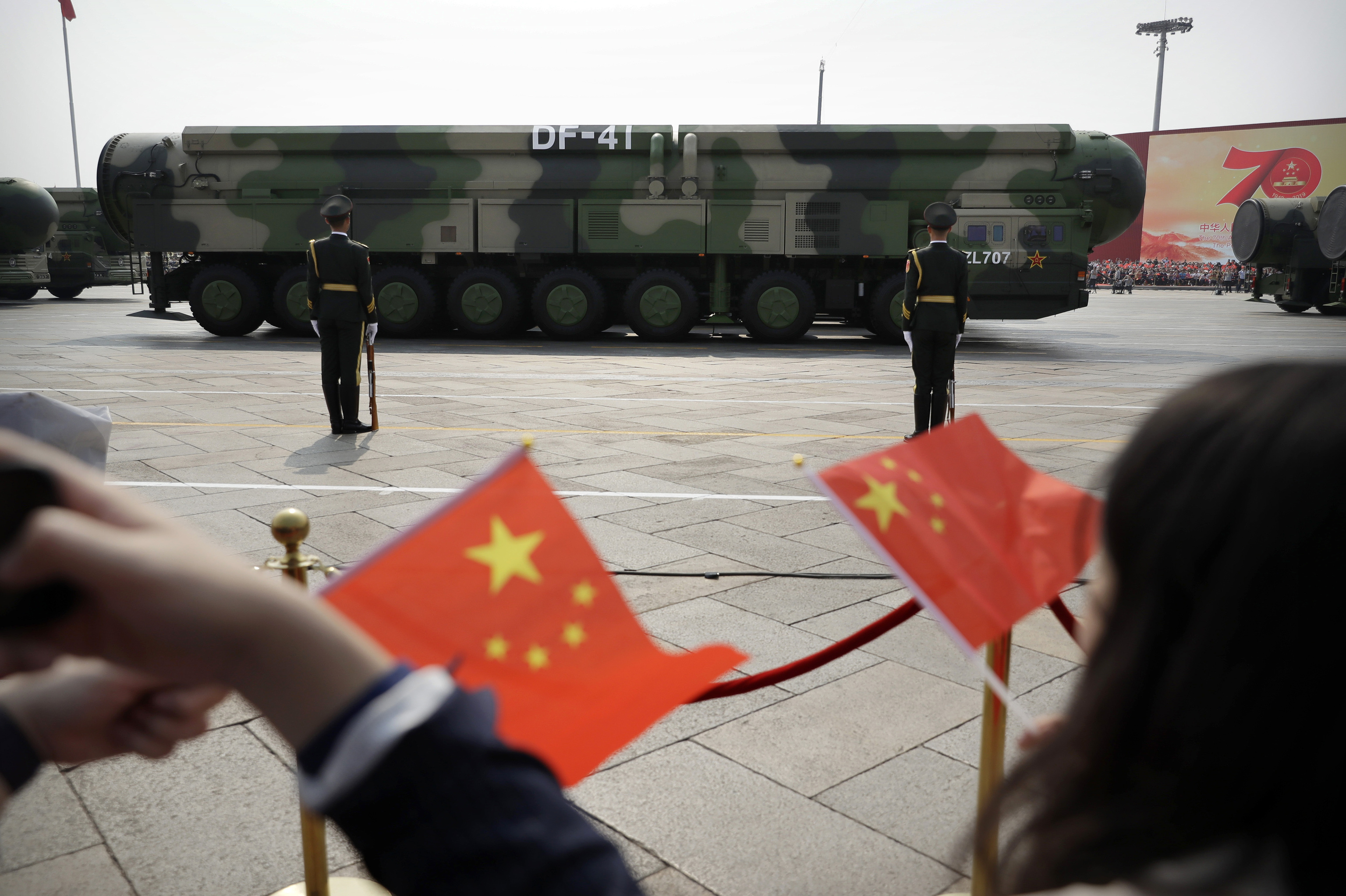 Espectadores agitan banderas chinas en un desfile militar.