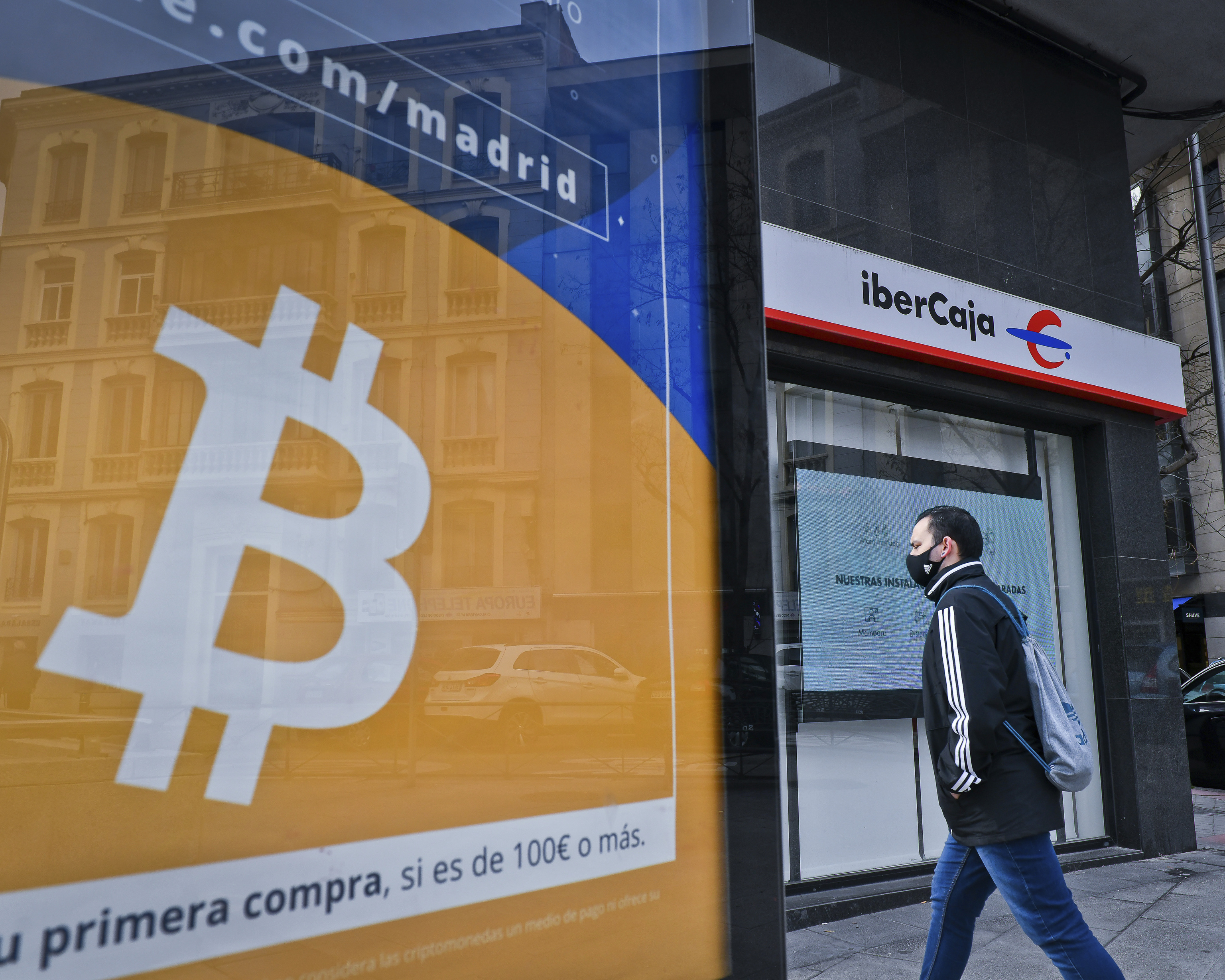 Un hombre pasa entre un anuncio para invertir en bitcoins y una sucursal bancaria.