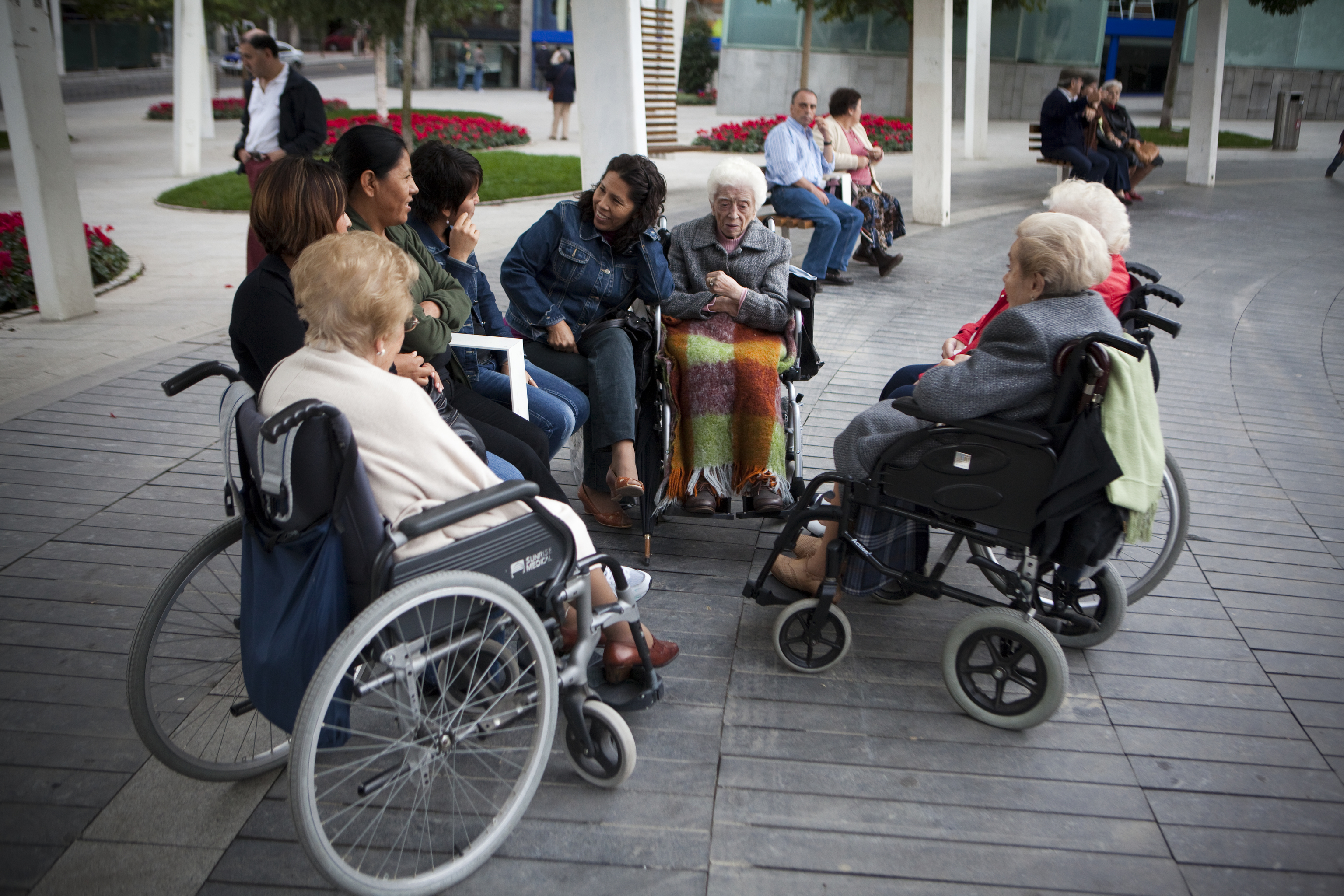 Ley de dependencia - mujeres inmigrantes latinoamericanas trabajan cuidando a personas mayores - ancianas - viejas - en silla de ruedas en el parque - trabajo - ancianos - vejez - minusvalia - cuidadoras