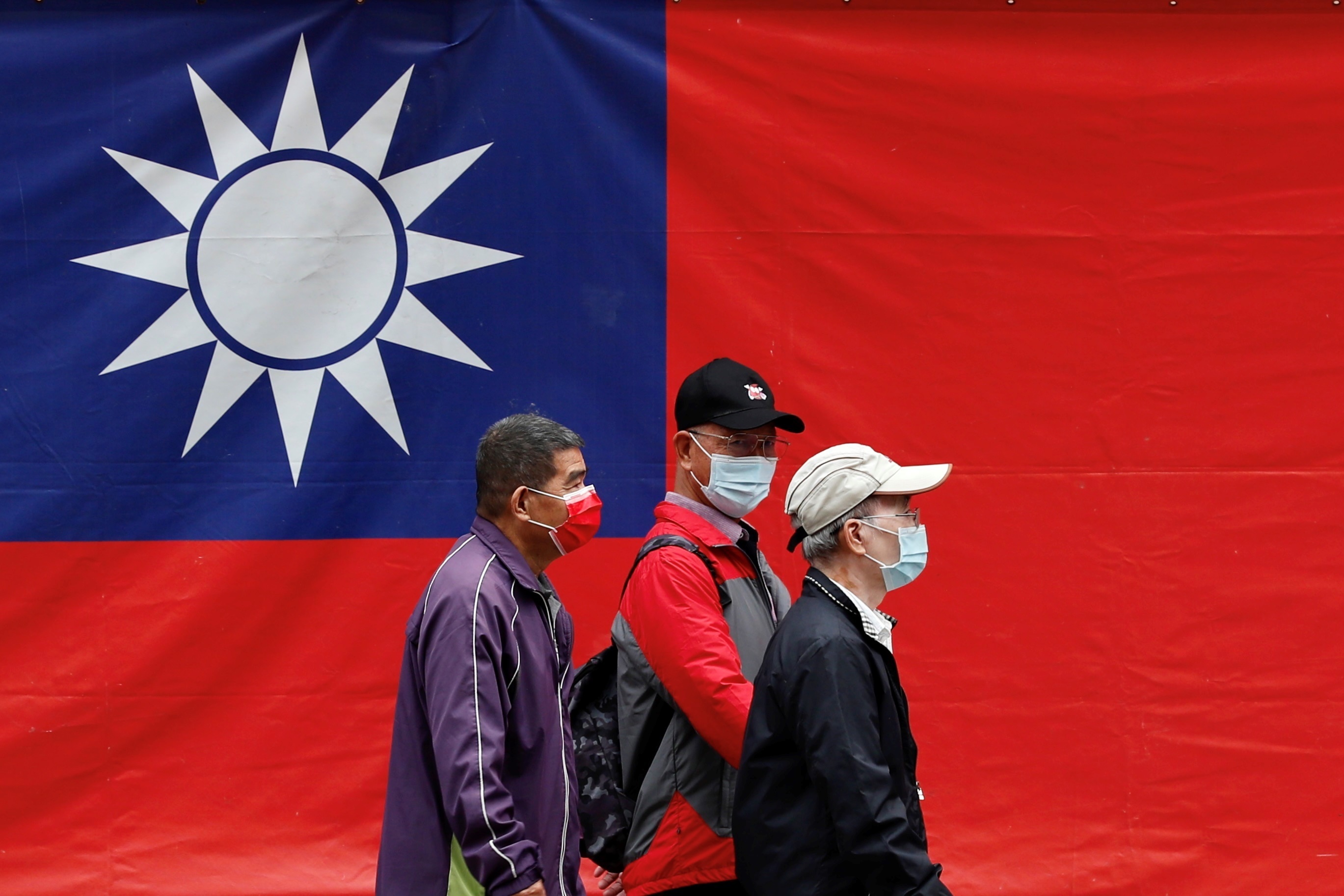 Varias personas caminan por delante de una bandera de Taiwan.