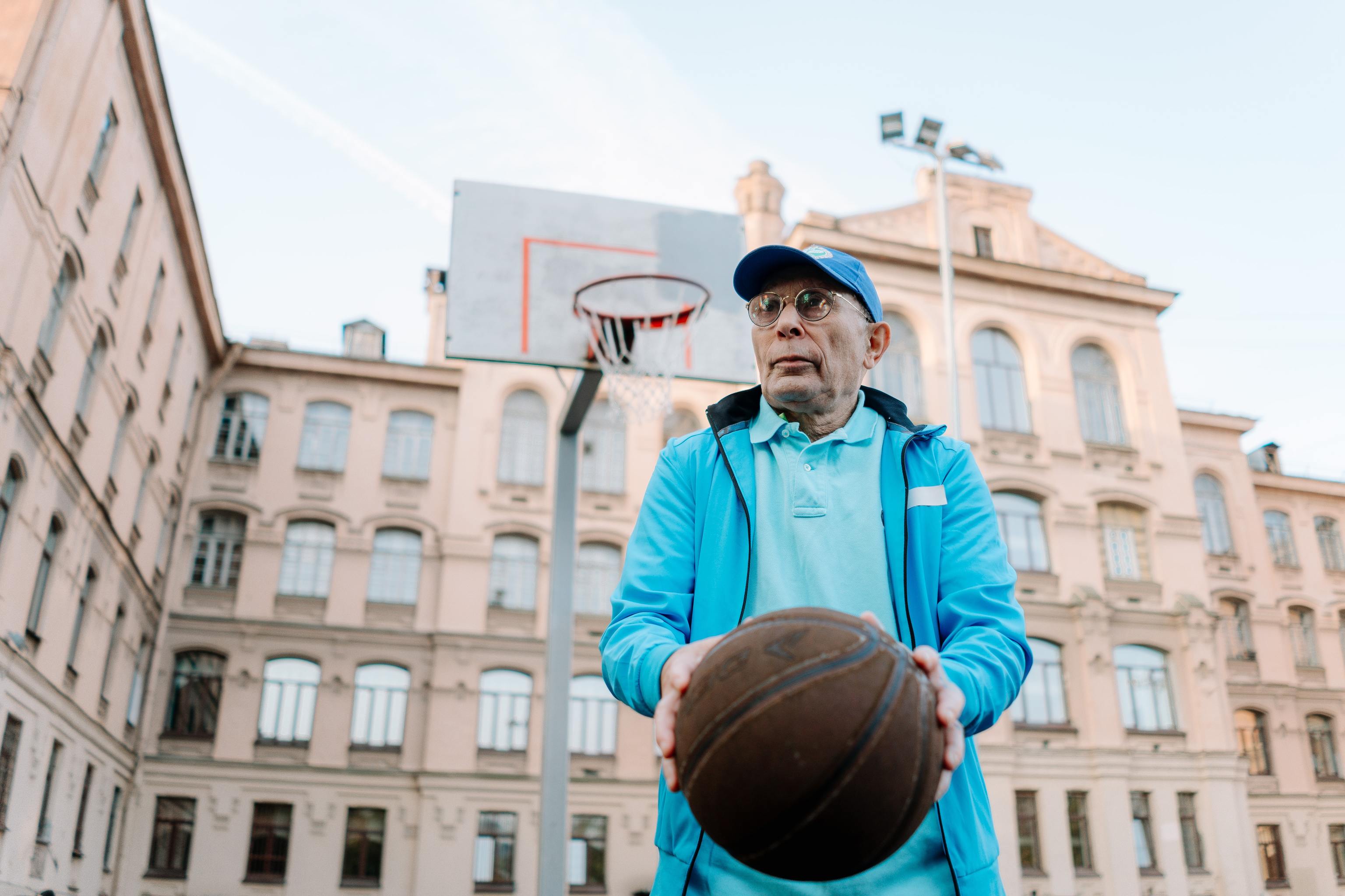 Un hombre jubilado sostiene un baln de baloncesto en una cancha ubicada al lado de un edificio.