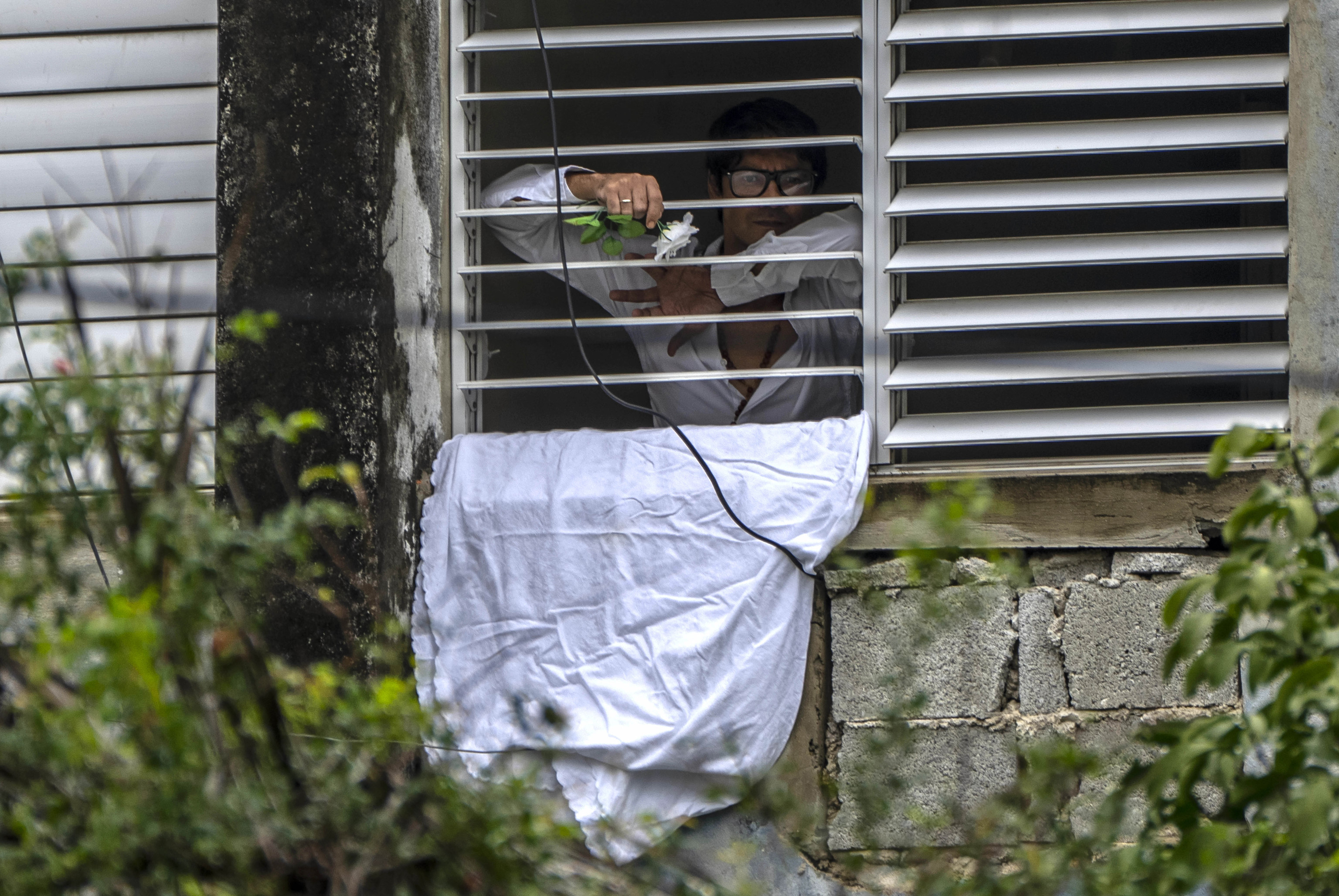 El opositor Yunior García Aguilera, bloqueado en su casa, enseña una flor blanca.