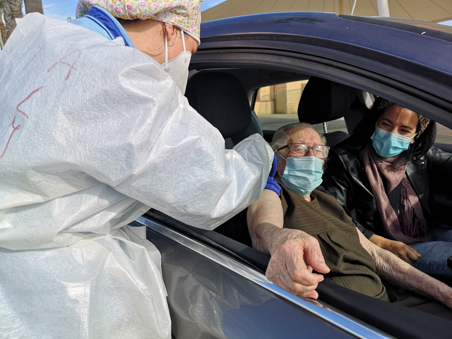 Un sanitario pone la vacuna a un hombre en el interior de su vehículo.