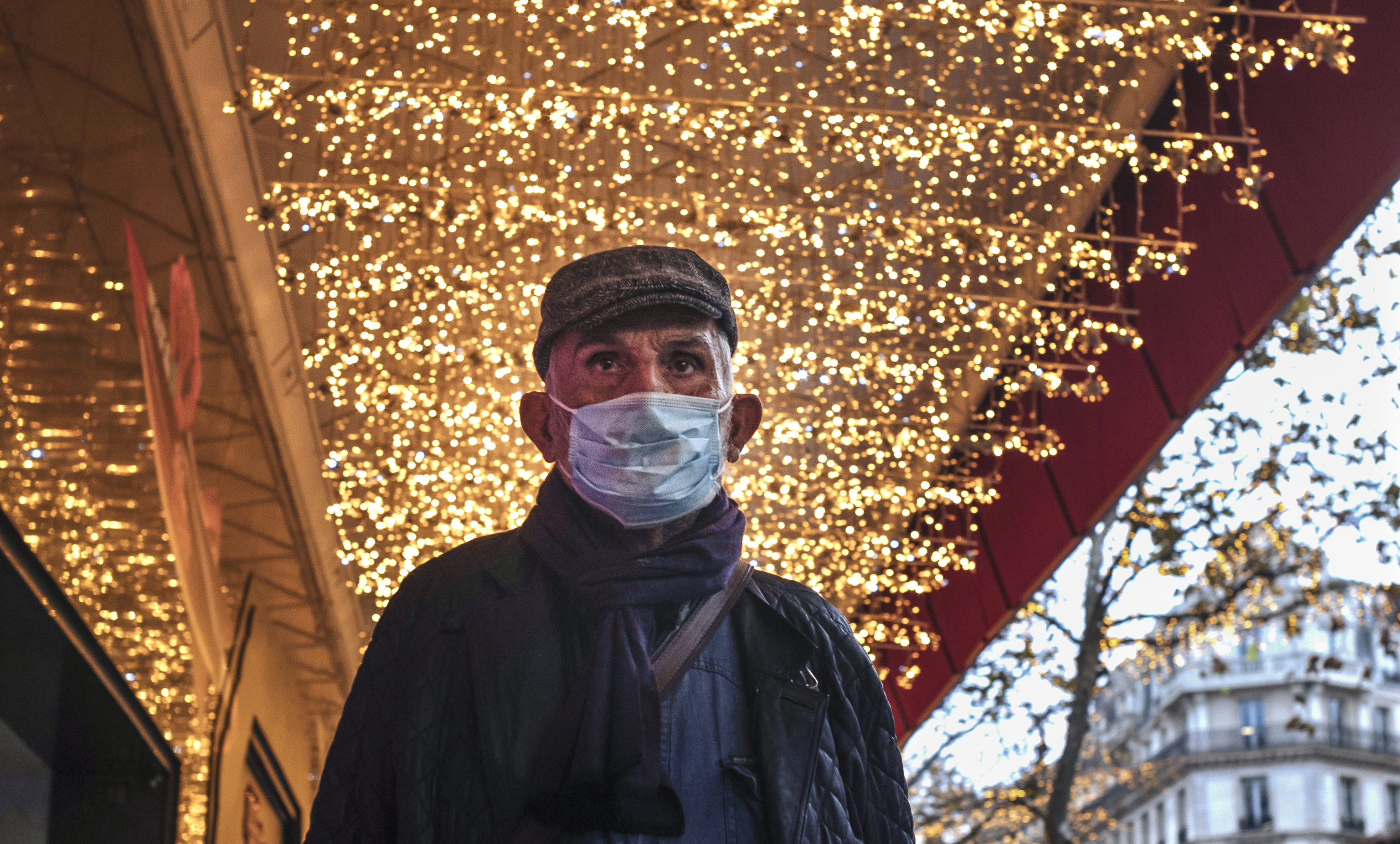 Un hombre lleva mascarilla mientras camina bajo unas luces de Navidad.