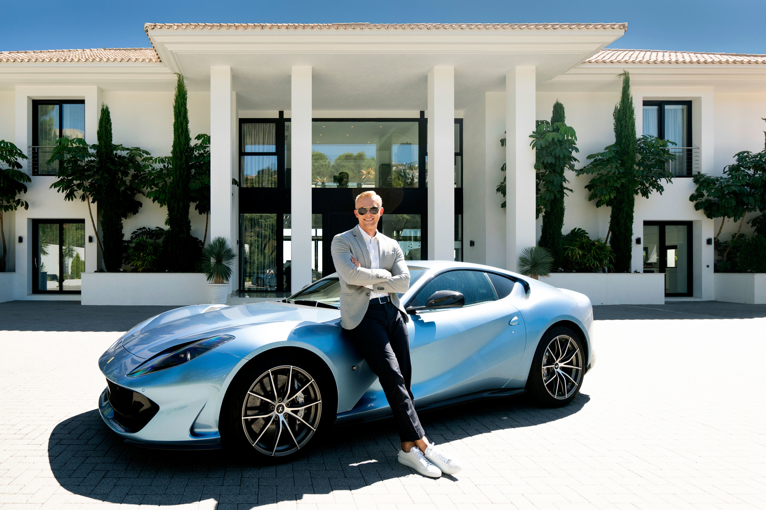 Artur Loginov posa con un Lamborghini frente a una de las casas que tiene a la venta.