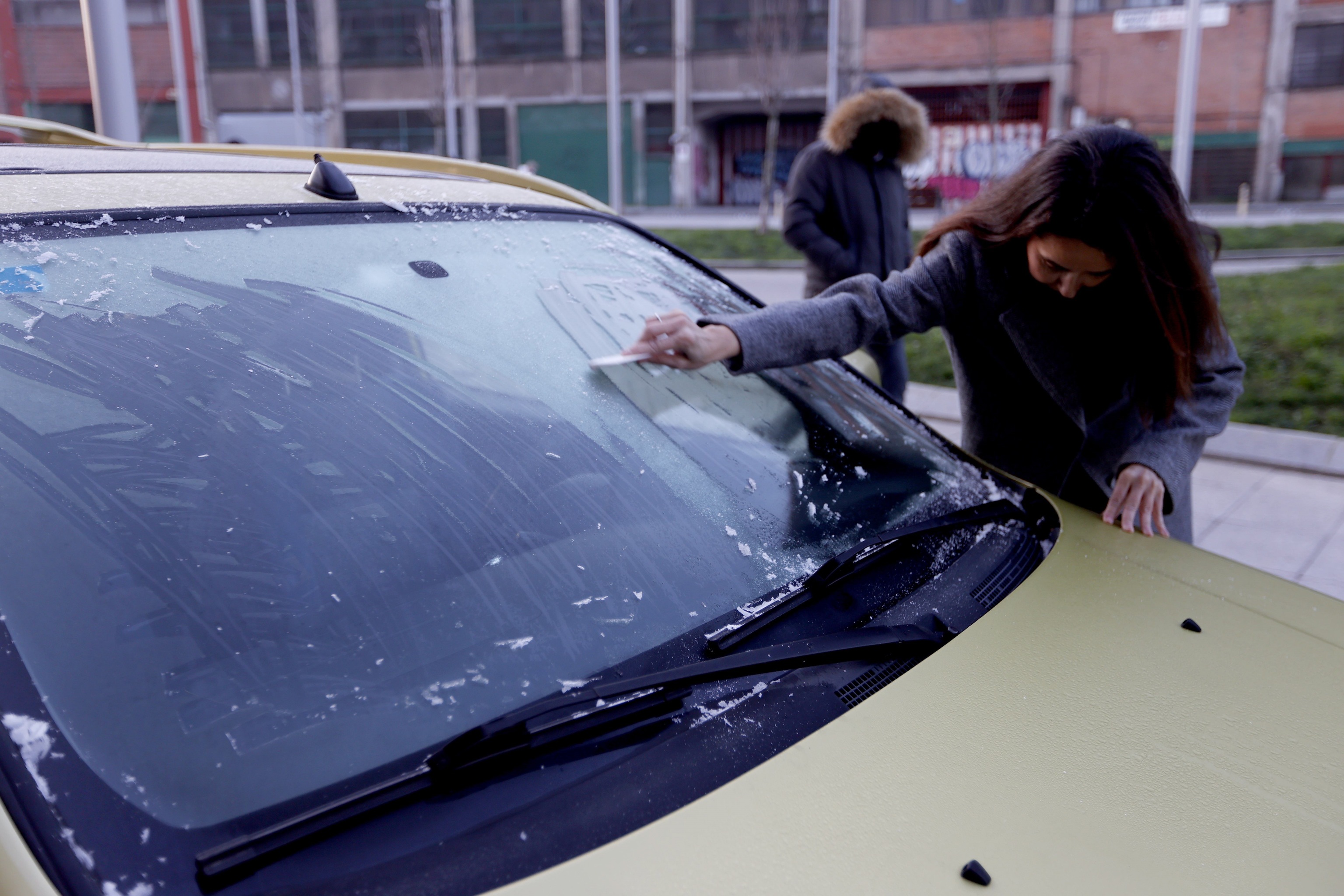 Una mujer retira el hielo de la luna del coche este martes en Bilbao, donde esta noche se han registrado fuertes heladas como consecuencia de las bajas temperaturas.EFE