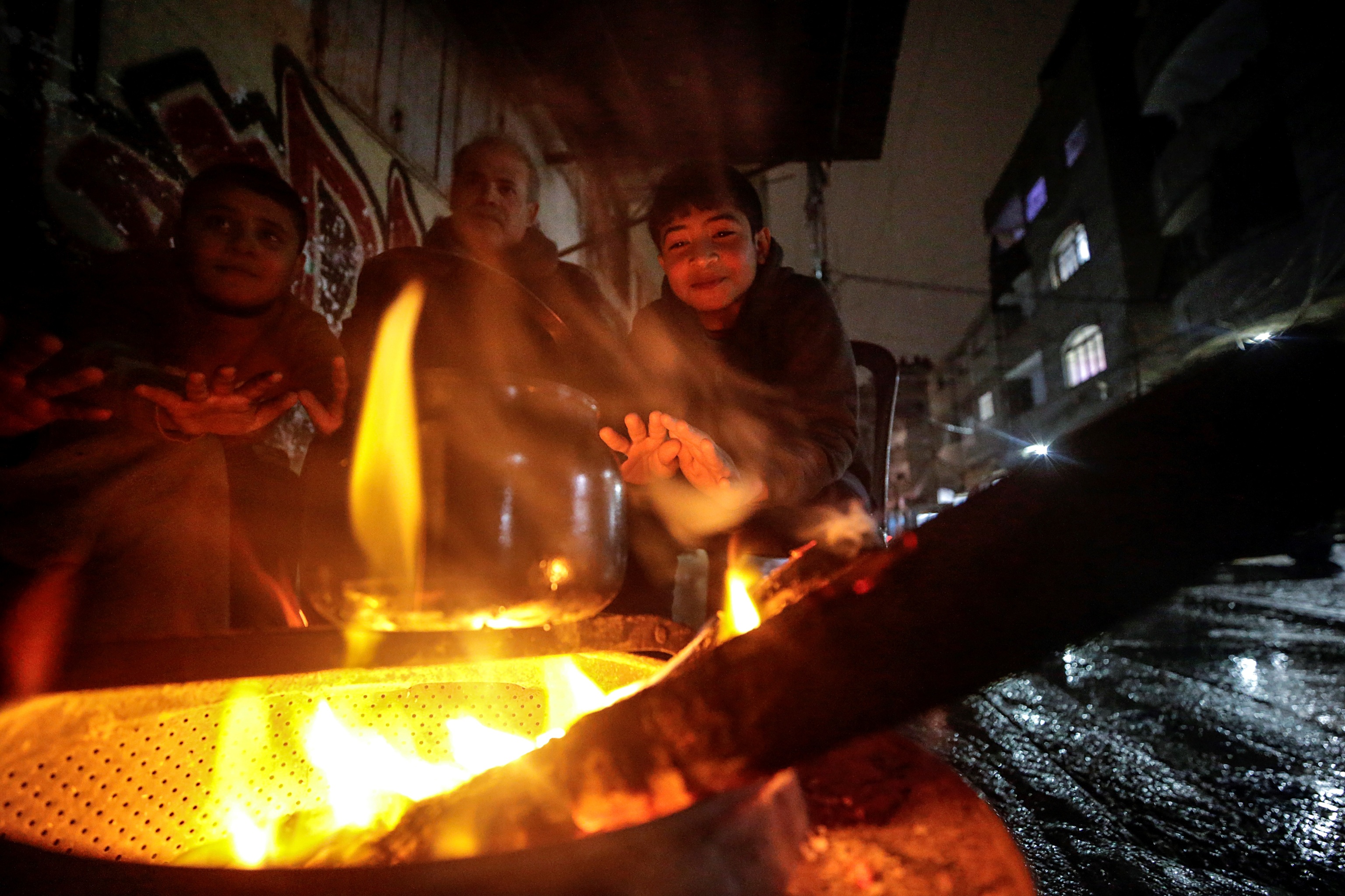 Refugiados palestinos se calientan en una fogata improvisada, en Gaza. t