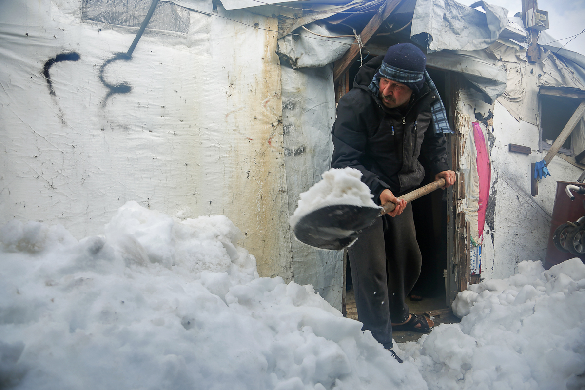 A Syrian refugee removes snow from the entrance to his tent in a camp in eastern L