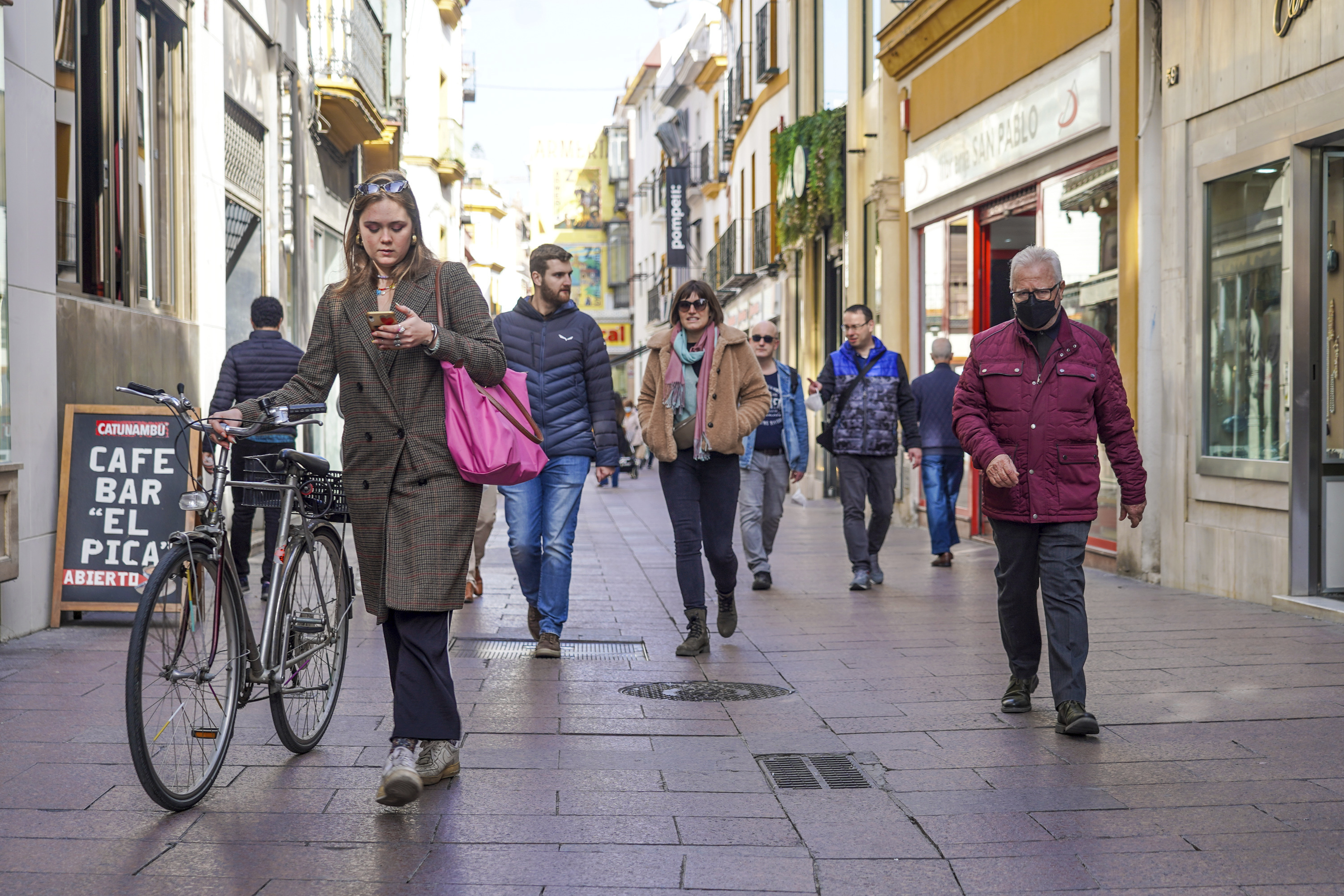Una mujer en bicicleta y otros ciudadanos sin mascarillas y otro con ella por la calle Sierpes.