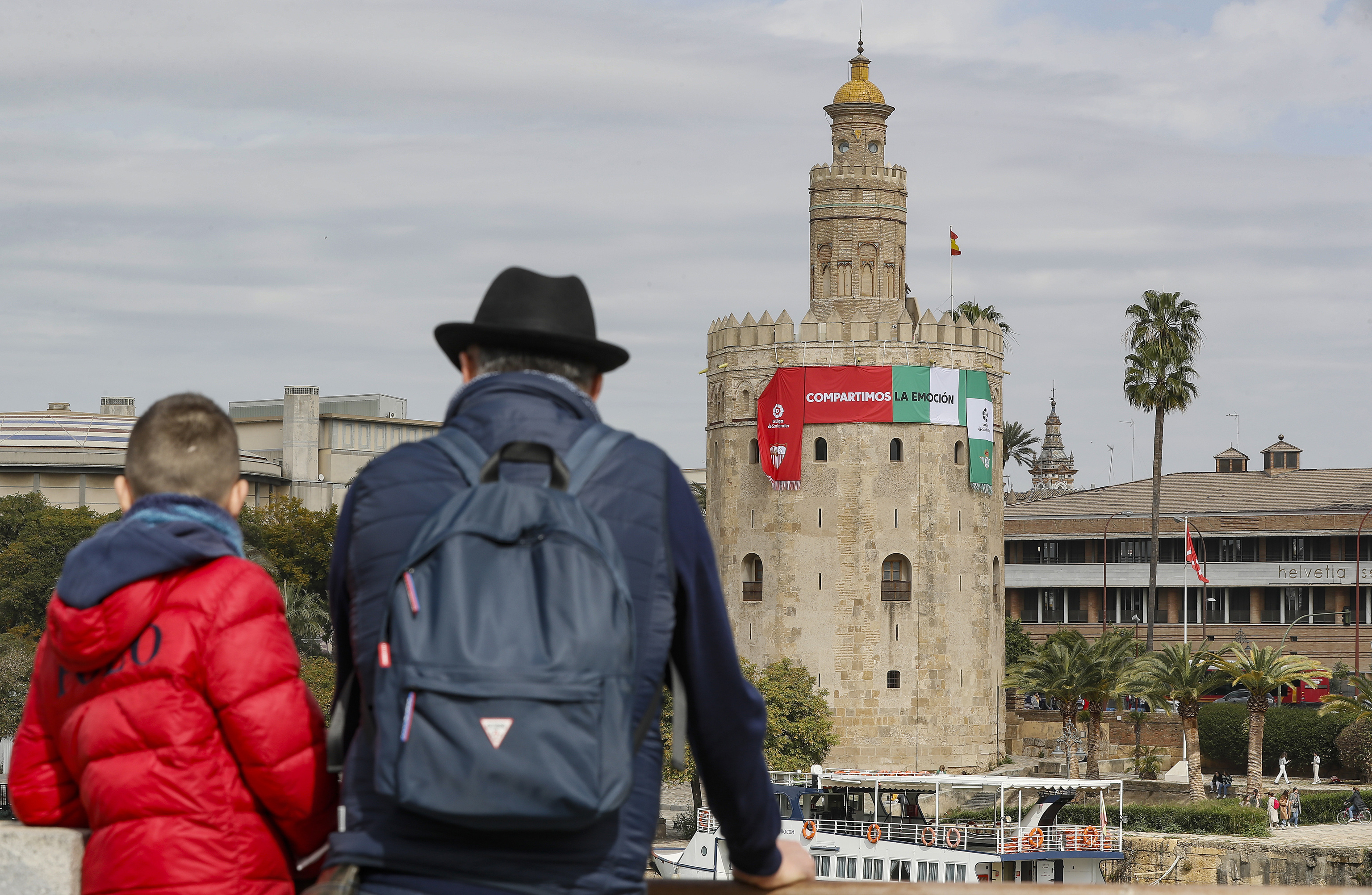 Dos aficionados observan la Torre del Oro, con las banderas de Betis y Sevilla.