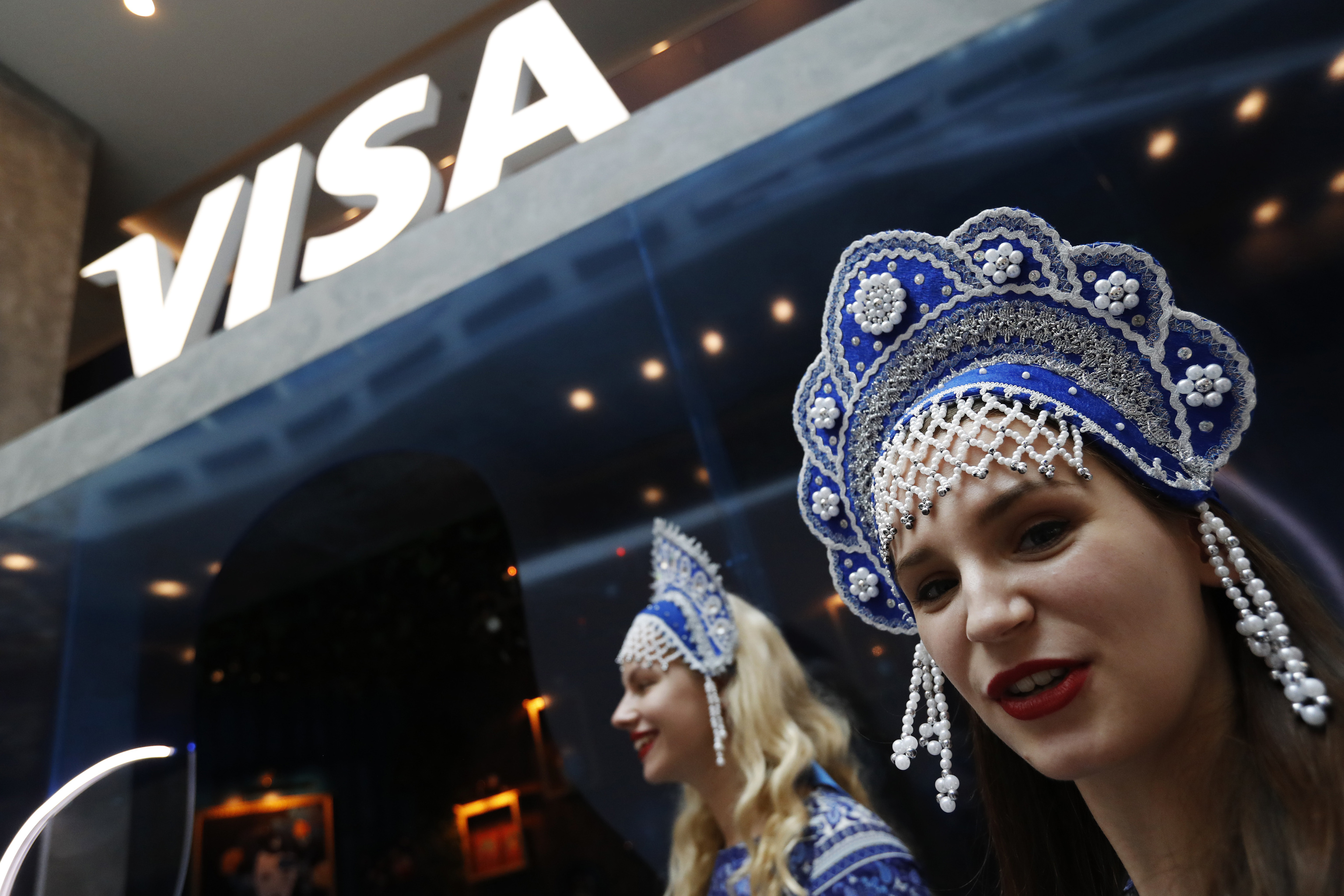 Imagen de julio de 2018: dosmujeres con la diadema tradicional reciben a los propietarios de tarjetas Visa que ganaron viajes al Mundial de Rusia.