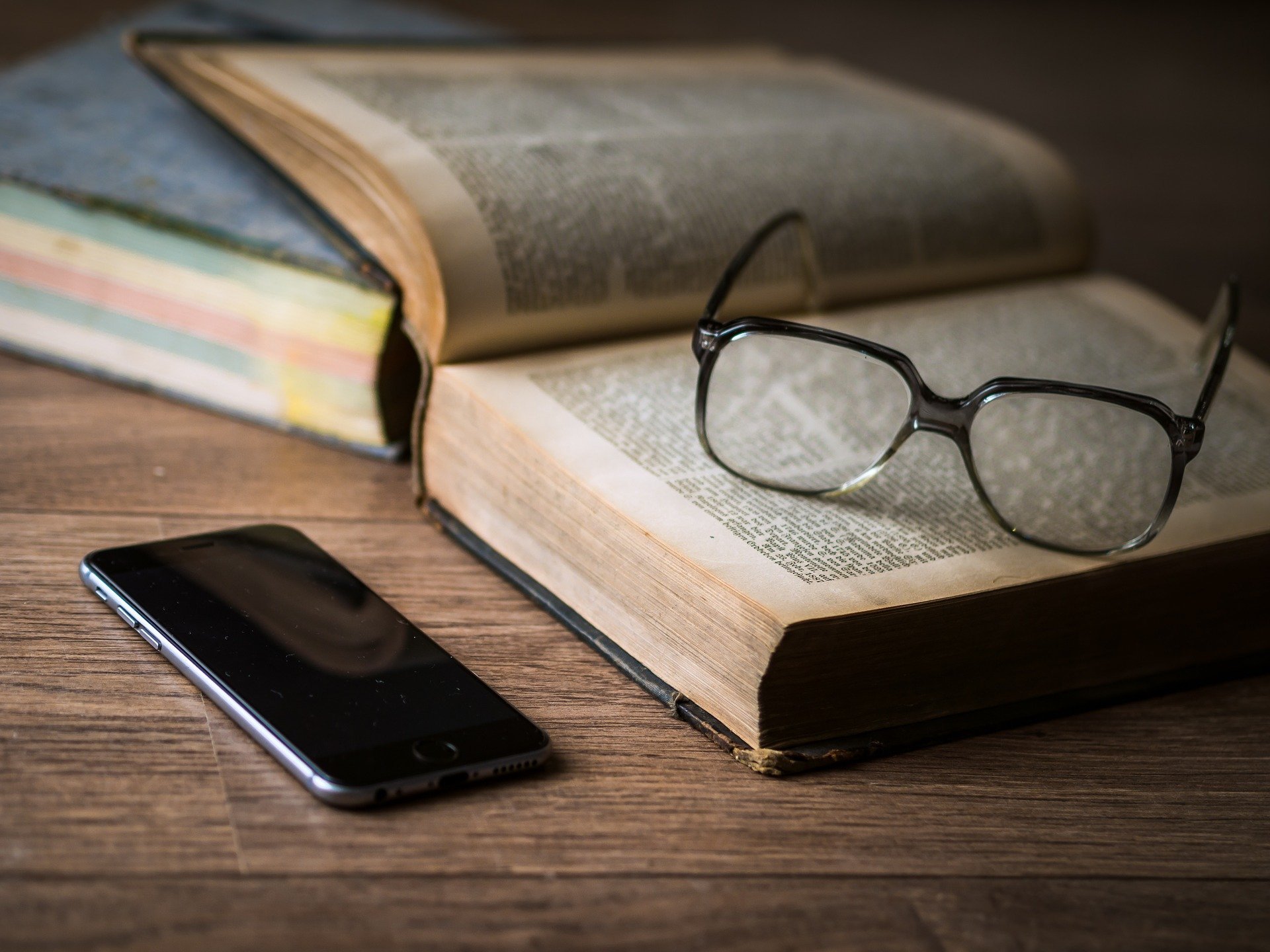 Un teléfono móvil, junto a un libro y unas gafas.