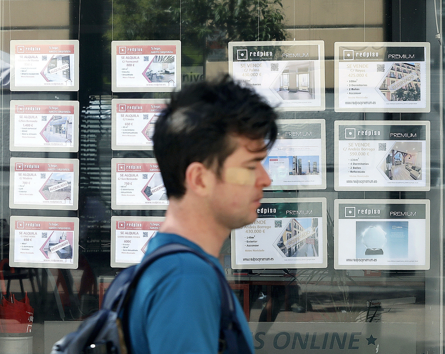 Un joven pasa por delante de una sucursal inmobiliaria de Madrid, con las ofertas en su escaparate.