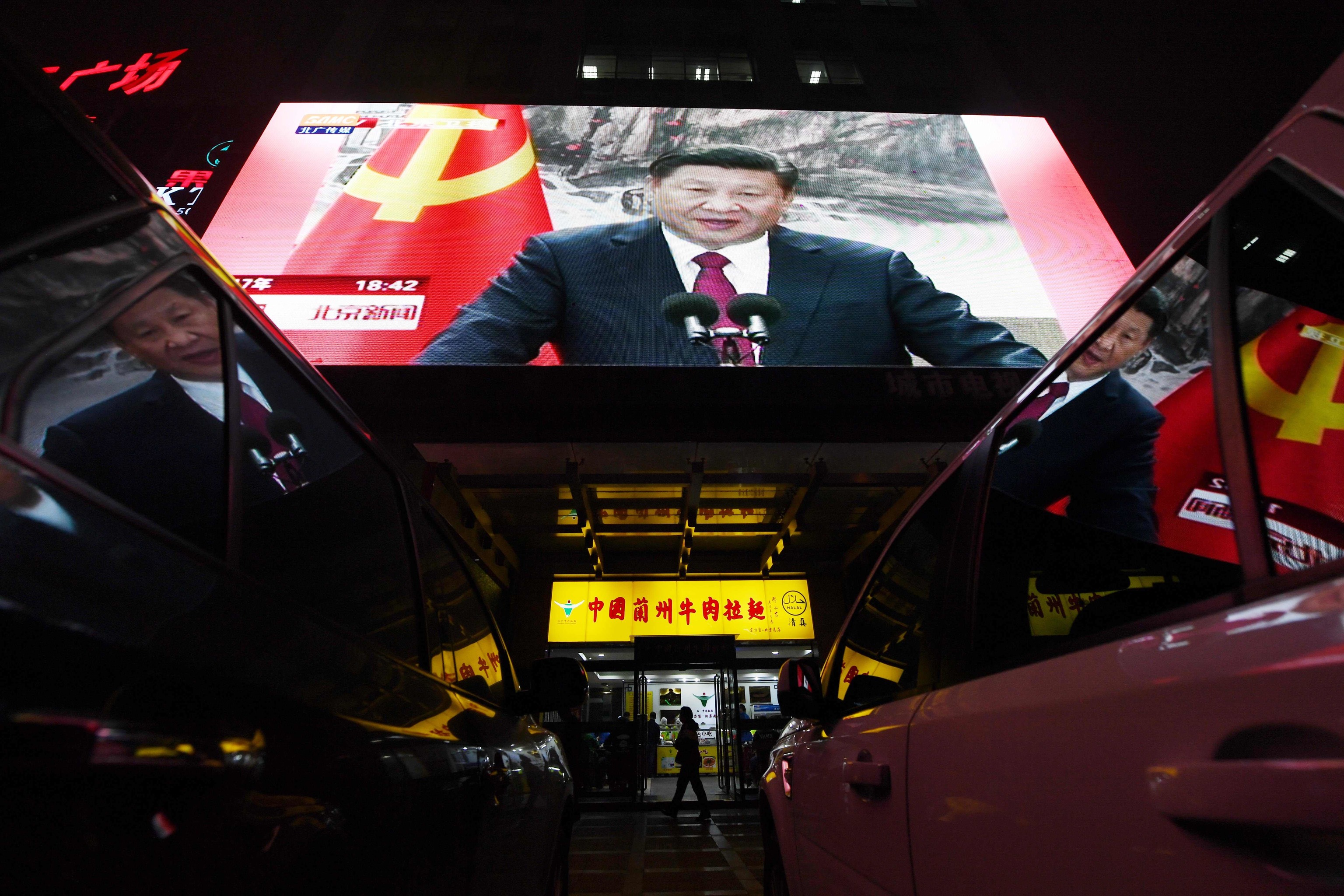 Gente pasa por delante de una tienda en la que hay instalada una gran pantalla en la que se muestra una intervención del presidente chino, Xi Jinping.