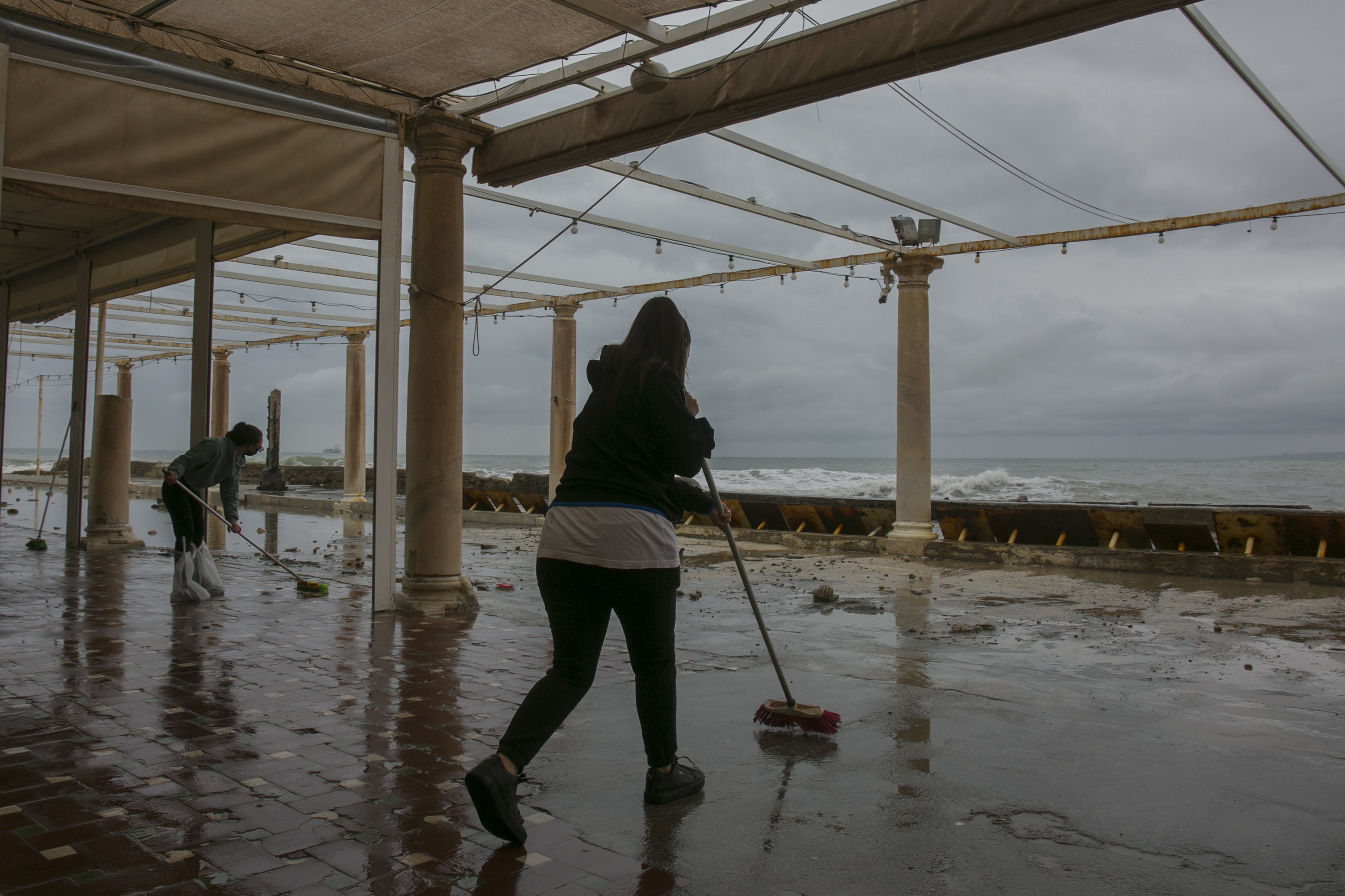Dos empleadas de una terraza limpian el barro y el agua dejados por el temporal en la zona de Baos del Carmen, en la capital malaguea.