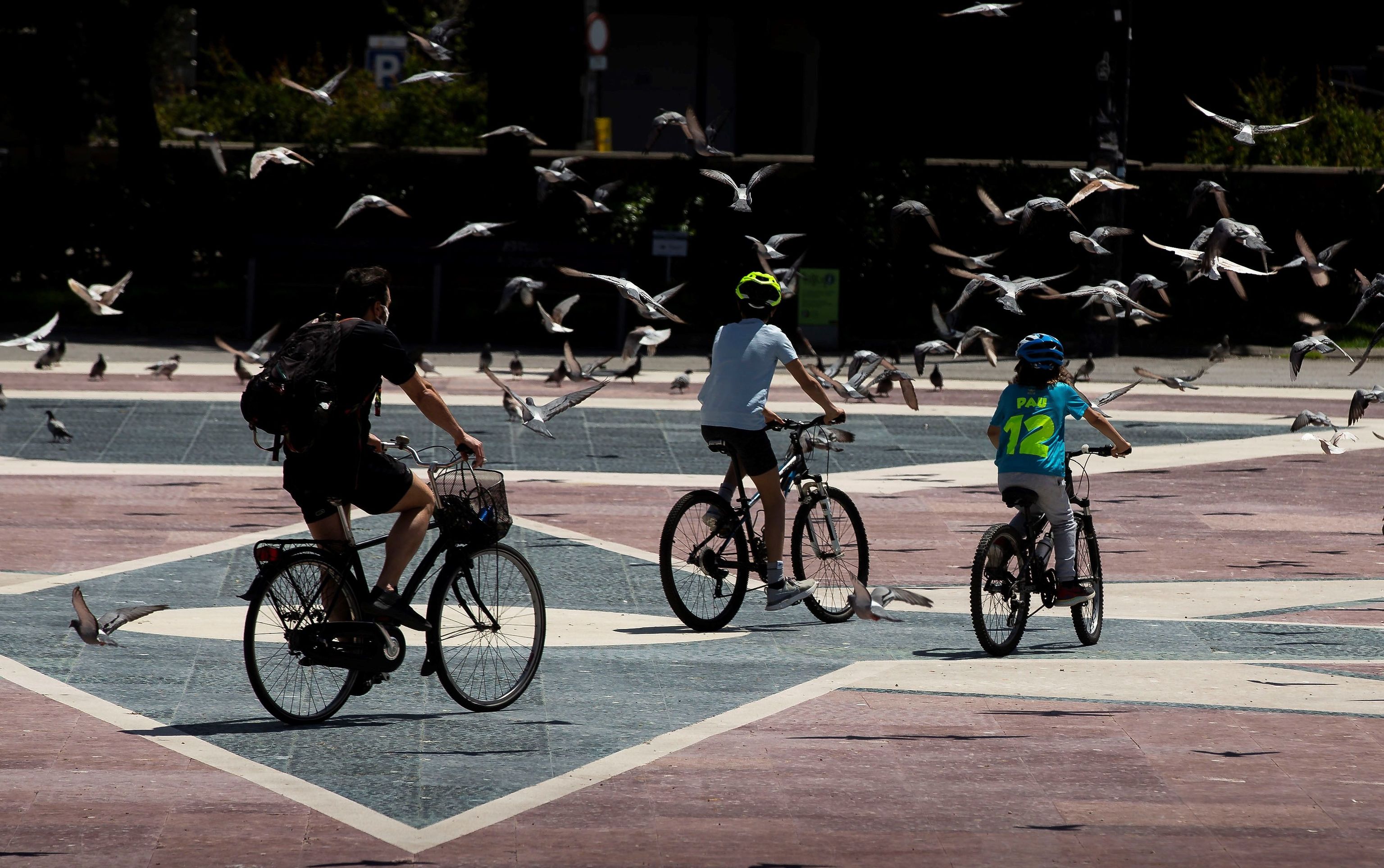 Dos nios y un adulto pasean en bicicleta por la Plaza de Catalua de Barcelona.