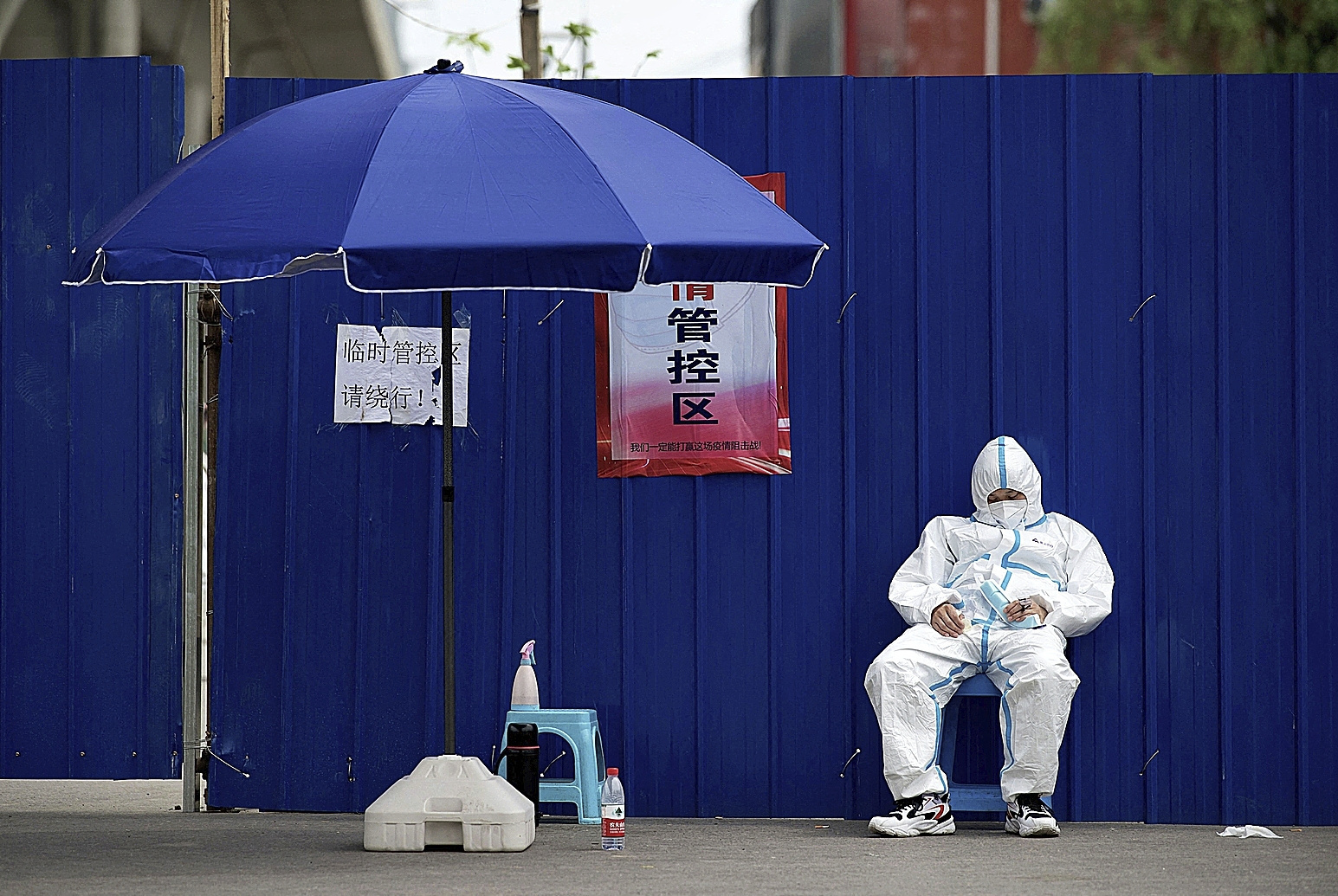 A security guard wearing PPE sleeps at the entrance of a confined compound in Beijing.