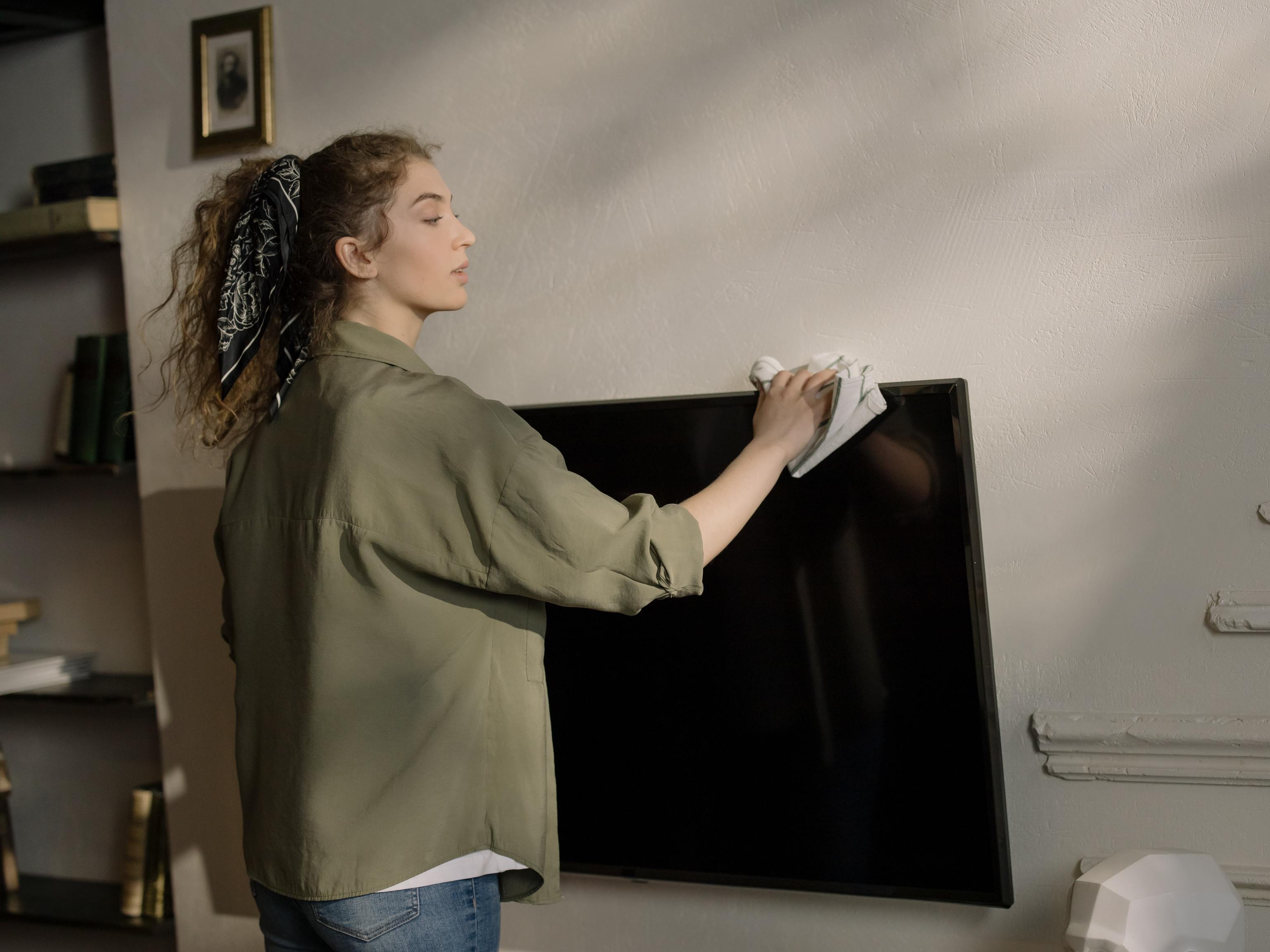 Una mujer limpia la pantalla del televisor con un paño.