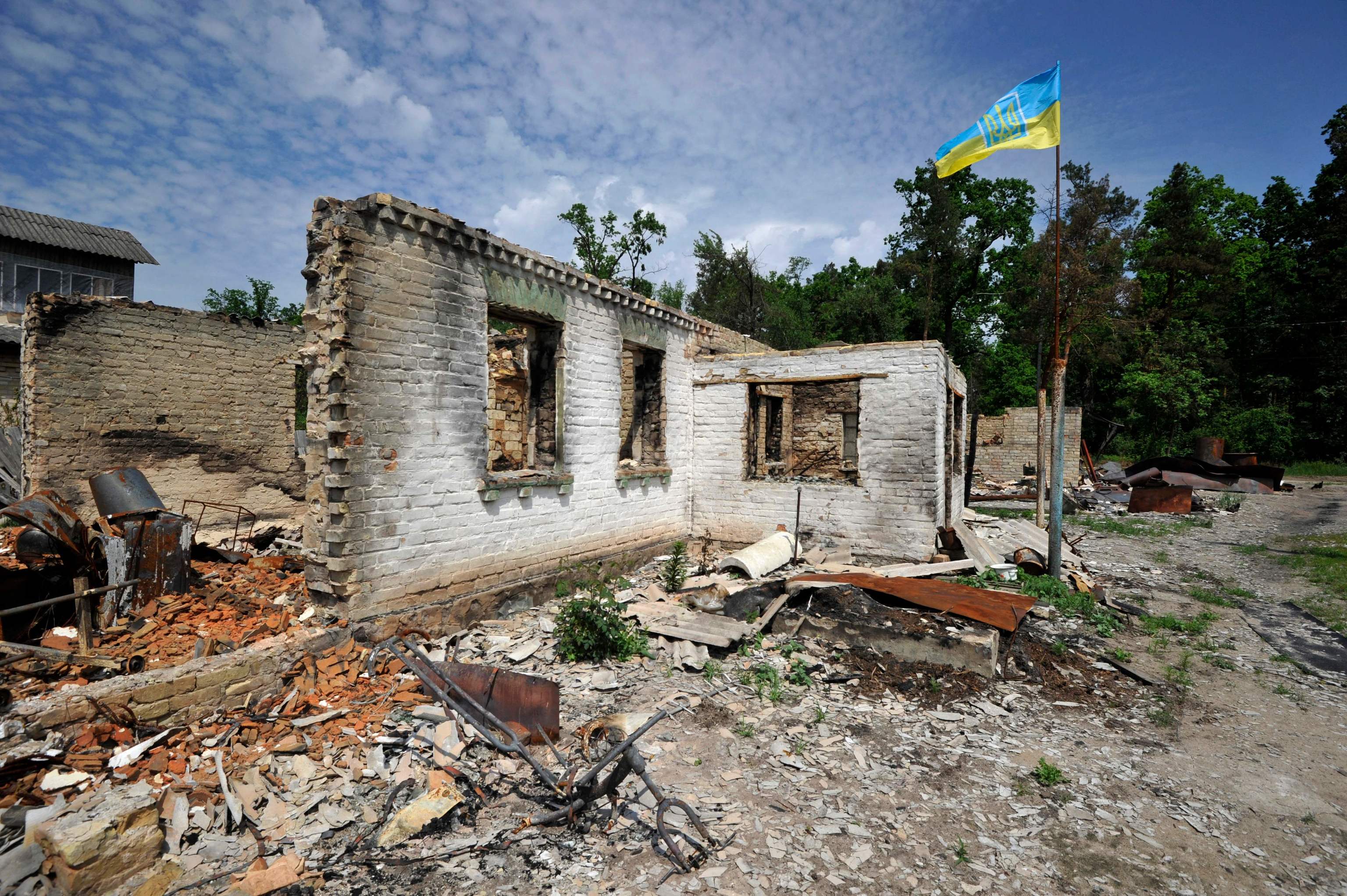 A Ukrainian flag flies over a destroyed house.